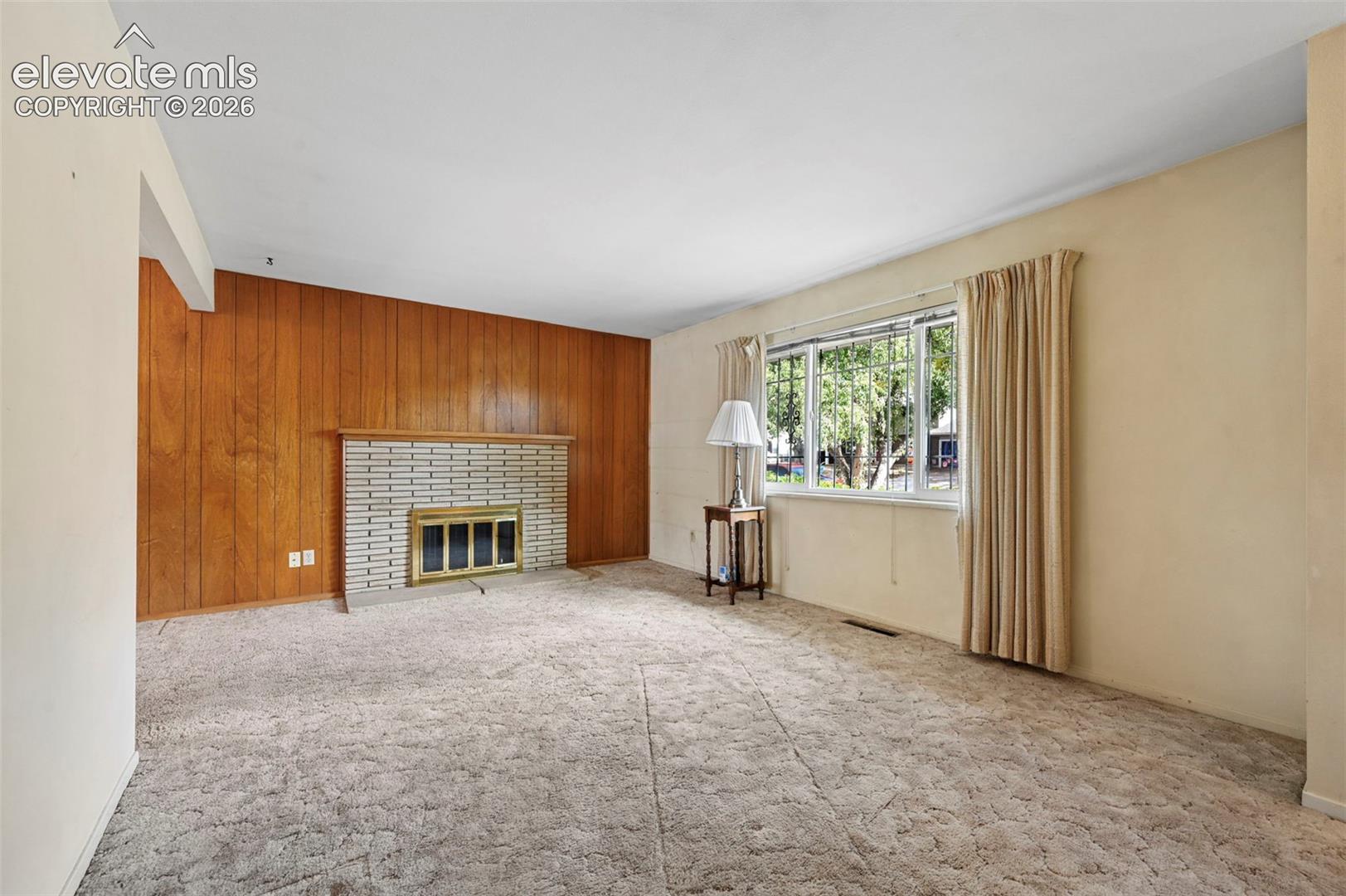 Living area featuring wood paneling, a floor-to-ceiling brick fireplace surround, a metal fireplace insert, and a large multi-pane window