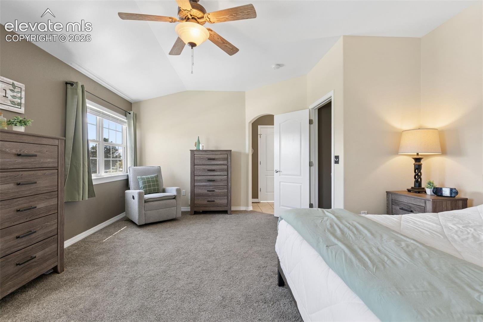Vaulted ceiling with a ceiling fan, carpeted flooring, and an arched doorway