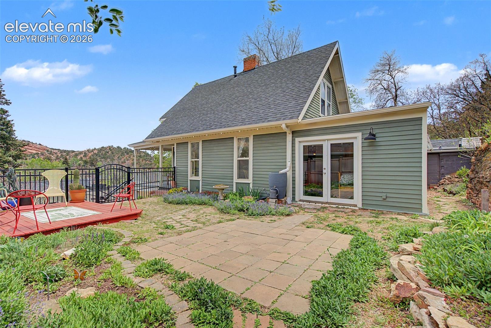 Exterior photo of structure featuring wooden deck, paved patio area, and double doors leading to the primary bedroom