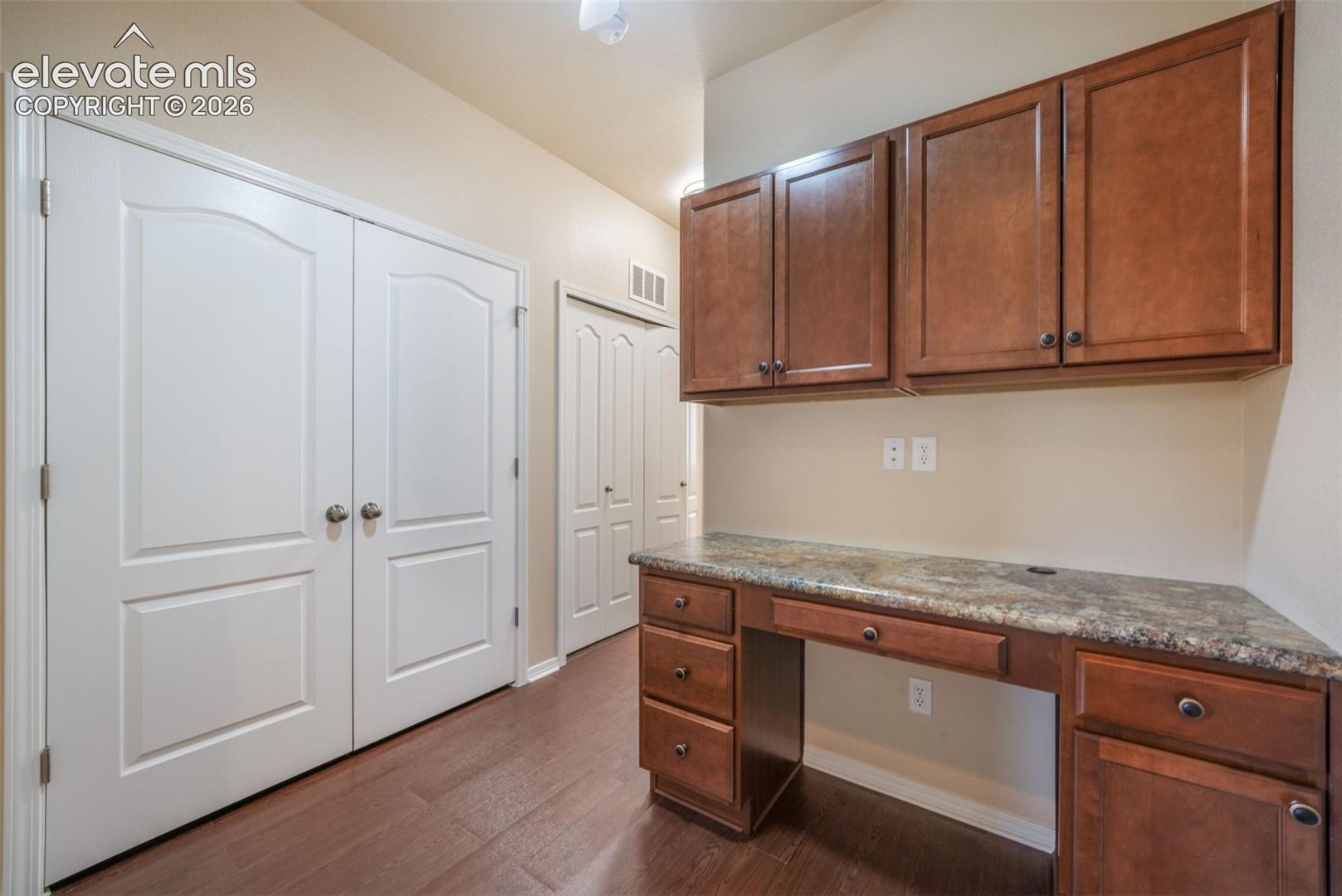 Built-in desk with a stone-finish countertop, wood-finish cabinetry, and wood-finish flooring