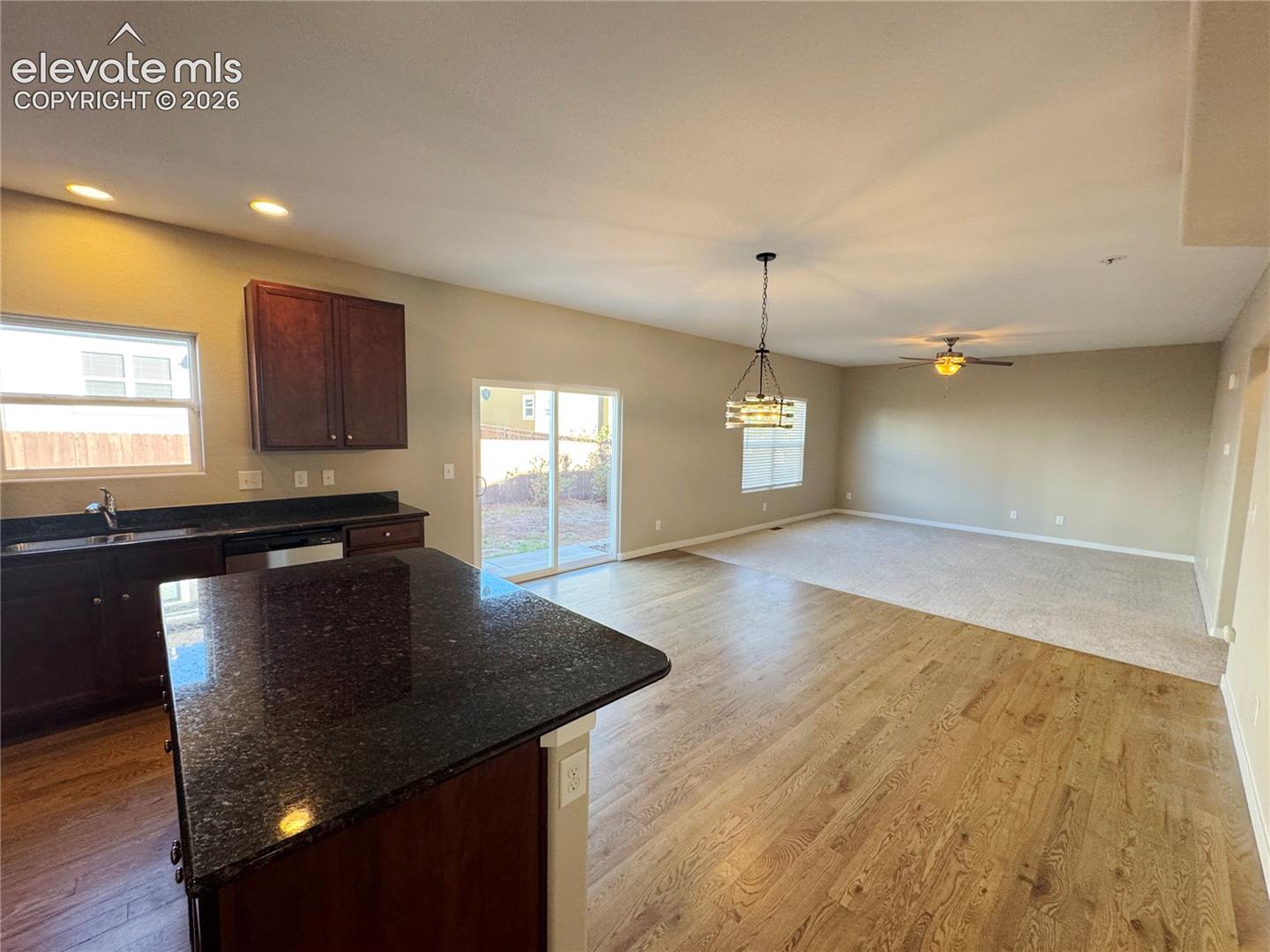 Kitchen area featuring a dark-finish kitchen island with stone countertop, wood-finish flooring, recessed lighting, multi-light chandelier, and glass sliding door
