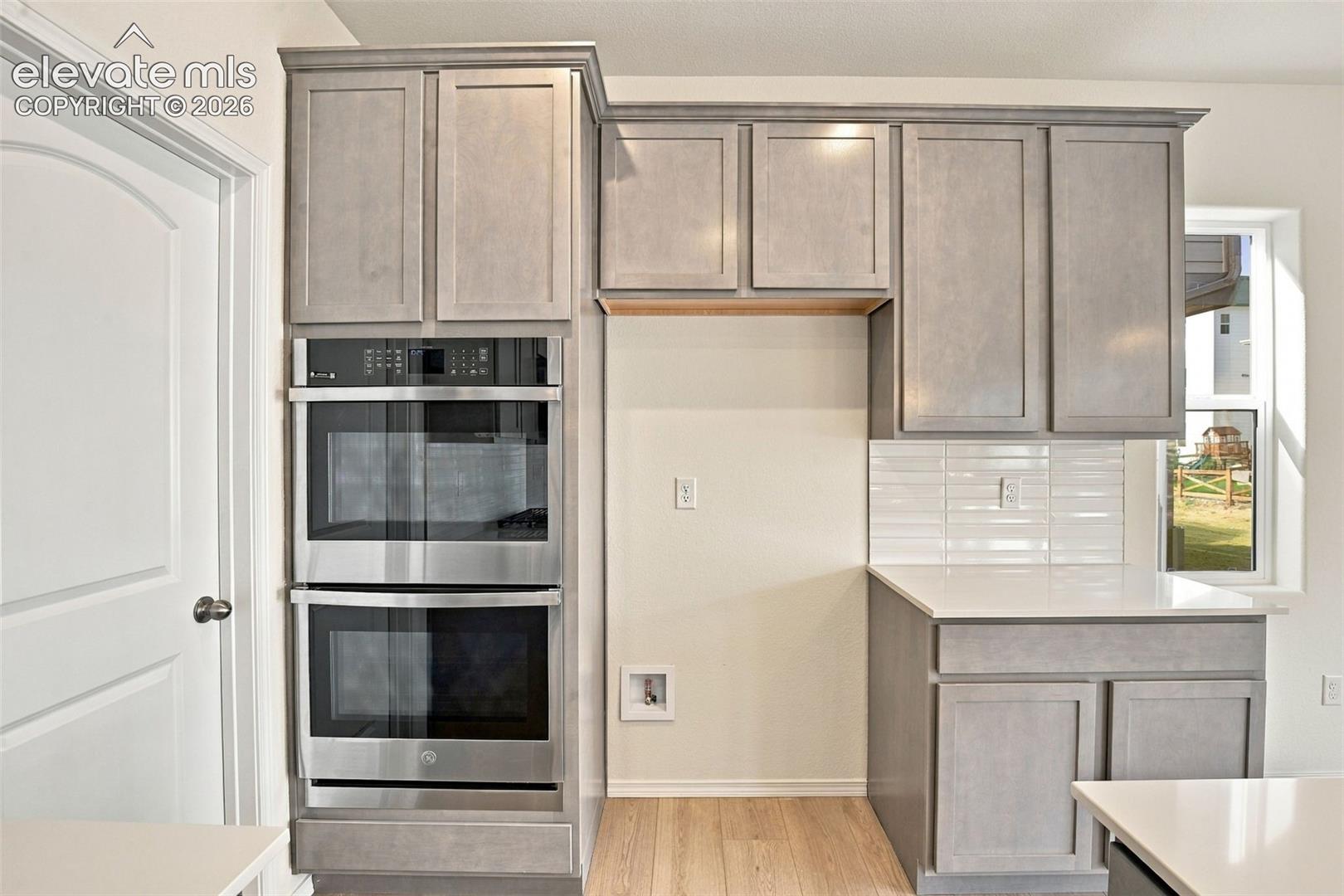 Kitchen cabinetry in a neutral finish, stainless steel double wall ovens, solid-surface countertops, and white subway tile backsplash