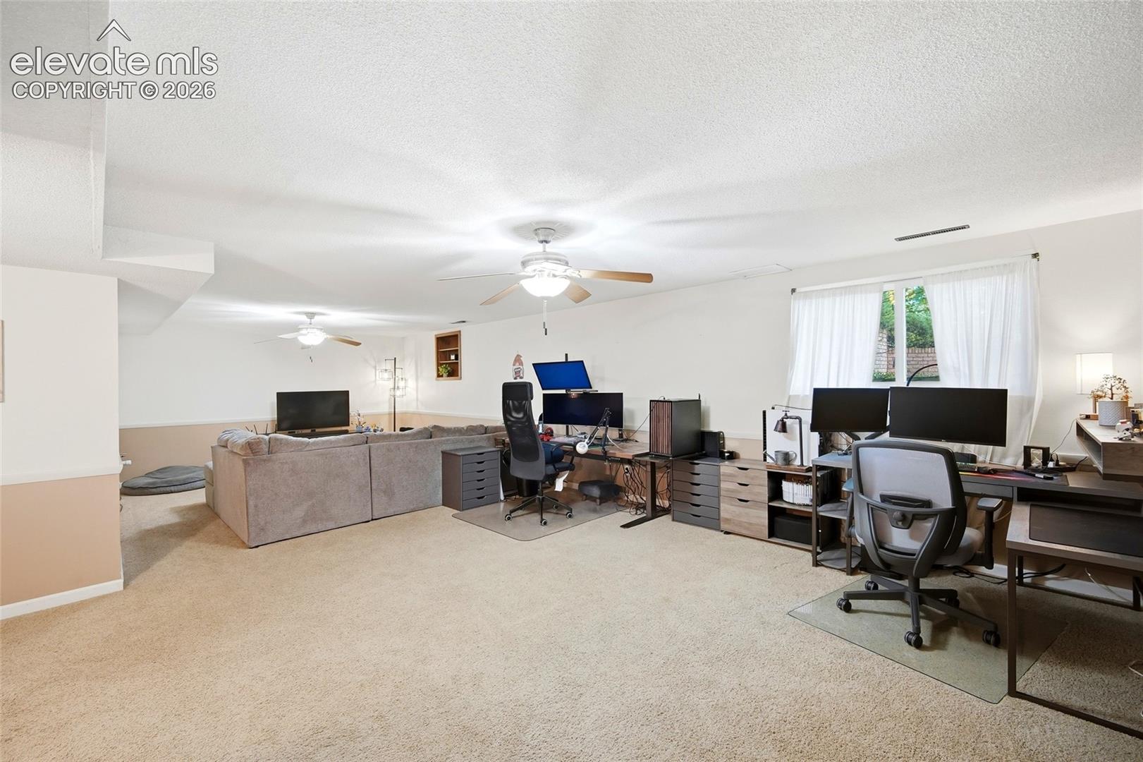 Neutral-toned carpeting, dual ceiling fans, recessed wall shelving, and large window with natural light