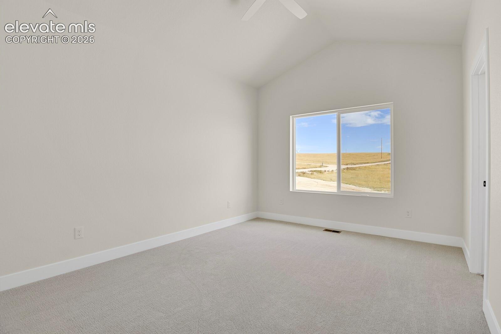 Vaulted ceiling featuring a central overhead fan, neutral wall finishes, carpeted flooring, and a large horizontal window