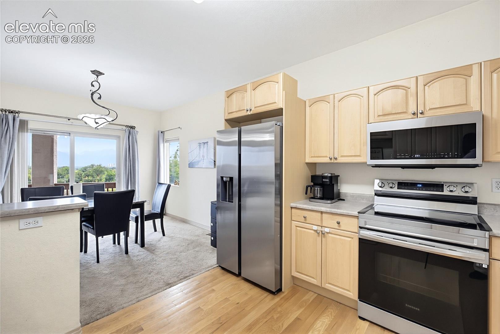 Kitchen featuring wood-finish flooring, light wood cabinetry, stainless steel appliances, and a double basin sink