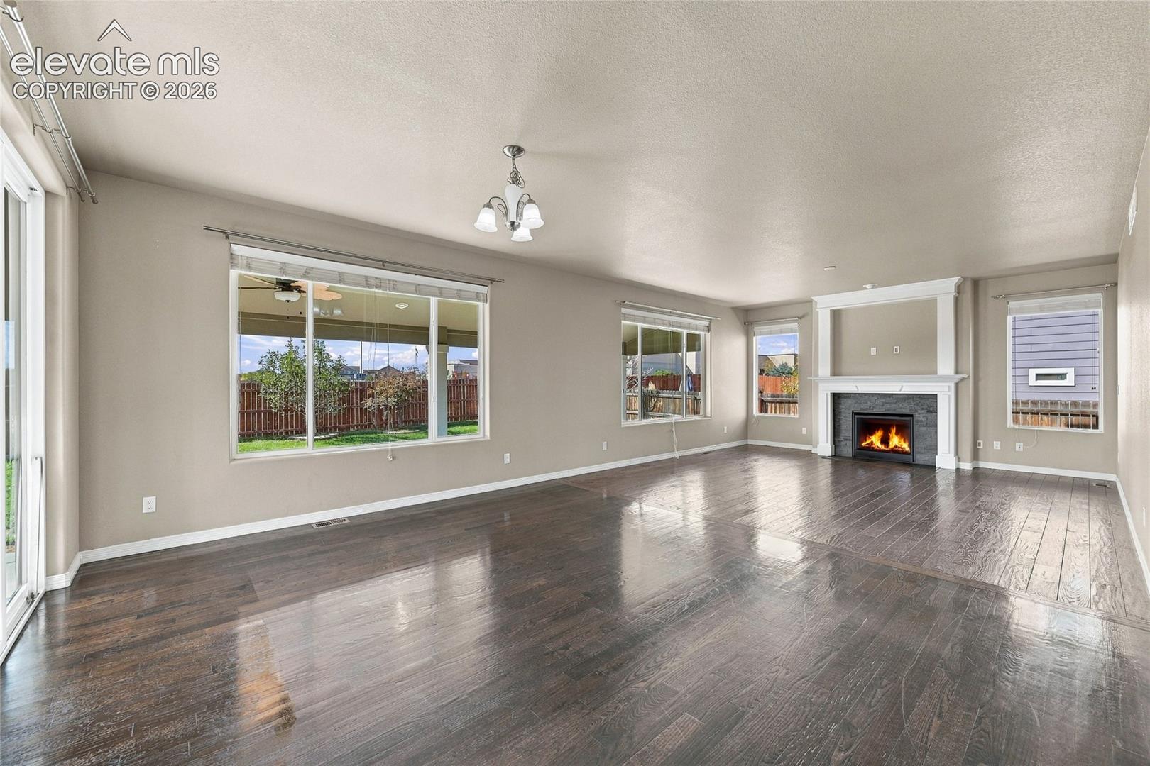Living area featuring wood-finish flooring, a fireplace with a decorative mantel and stone-tile surround, multiple windows, and a multi-arm chandelier