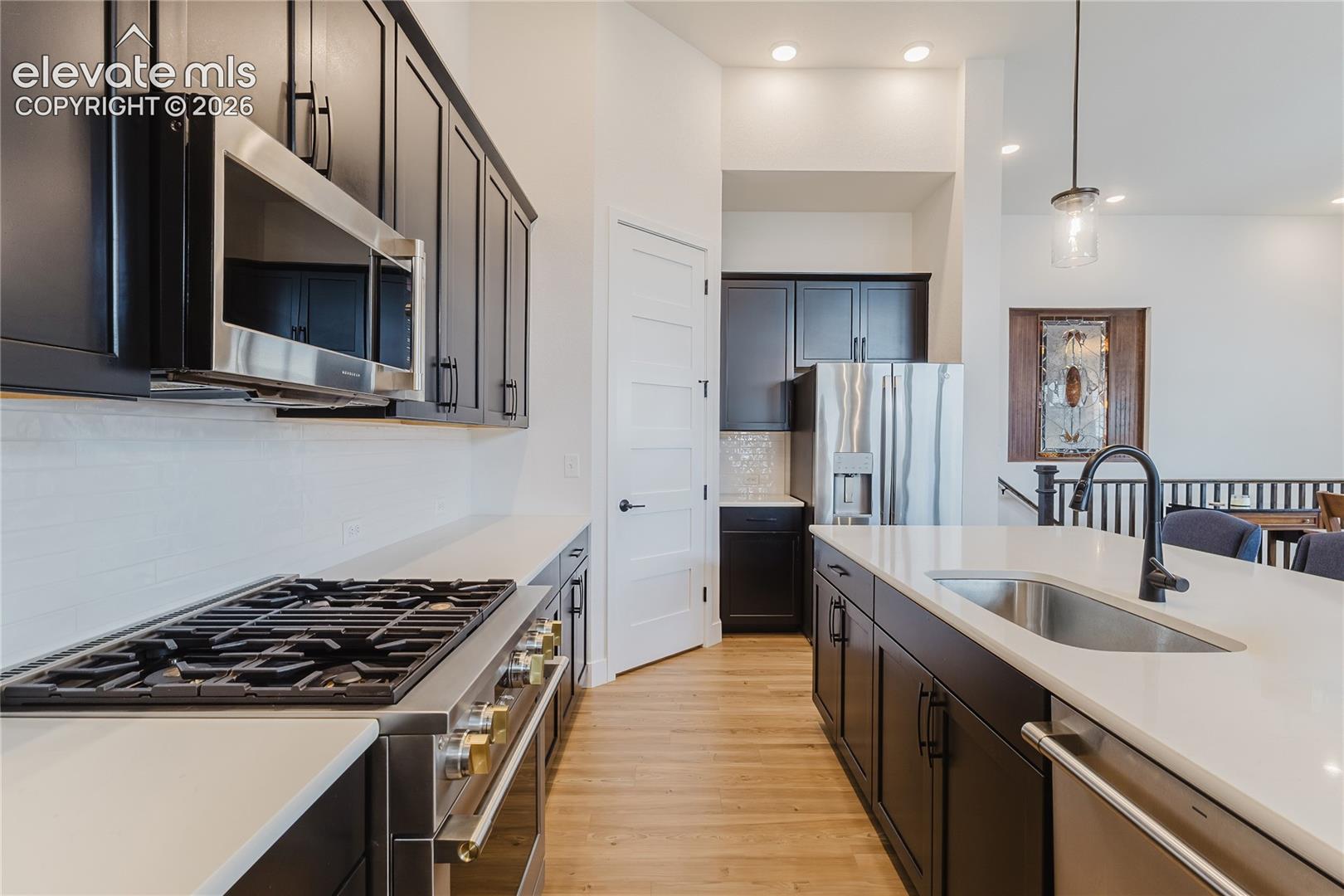 Gourmet kitchen featuring dark wood cabinetry, stainless steel appliances, a gas range 4' x 8' island with an undermount sink and matte black faucet ad walk-in pantry