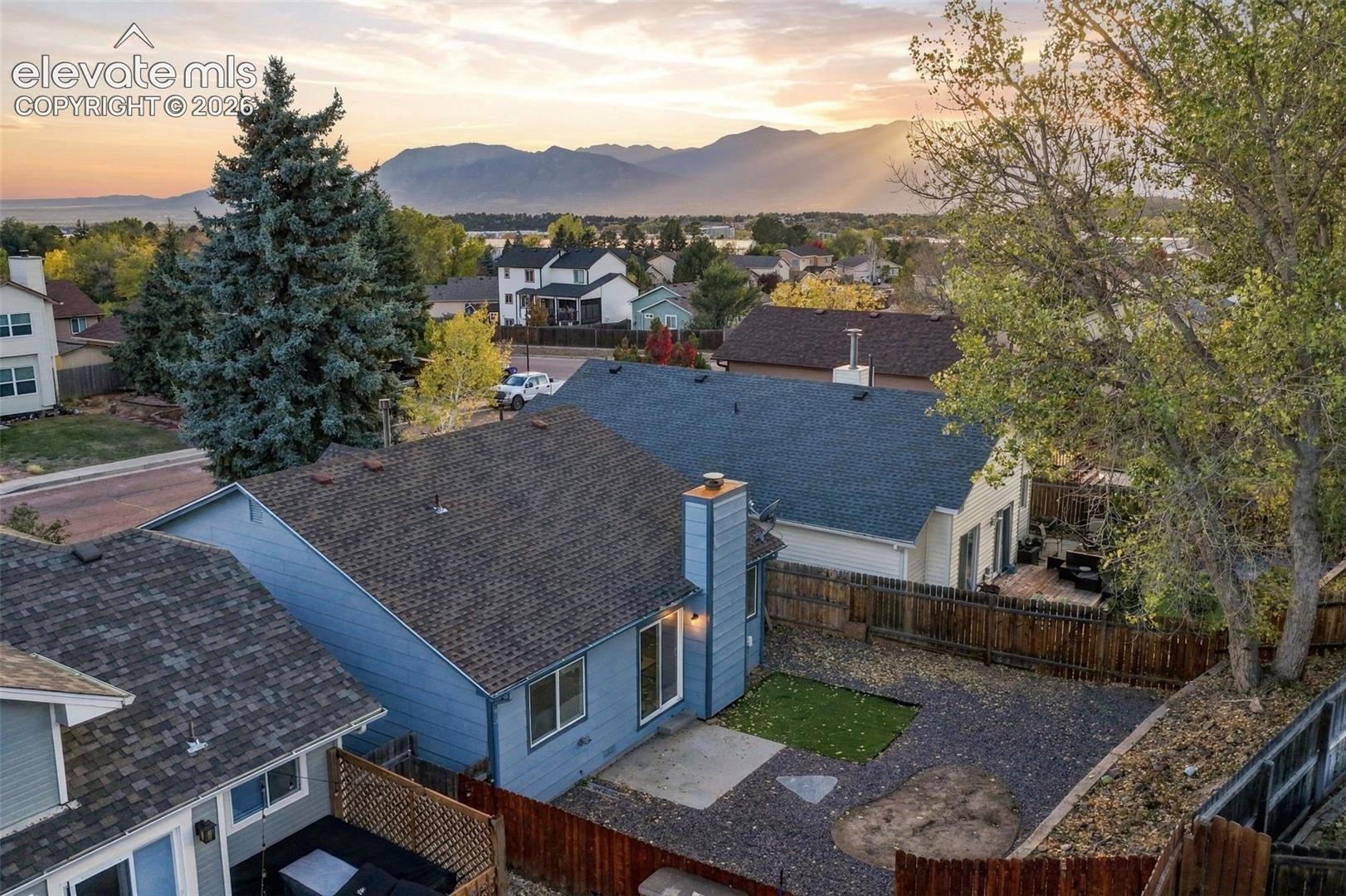 Exterior aerial perspective featuring a fenced backyard with hardscaping, a concrete patio, a central lawn area, and a prominent mountain backdrop