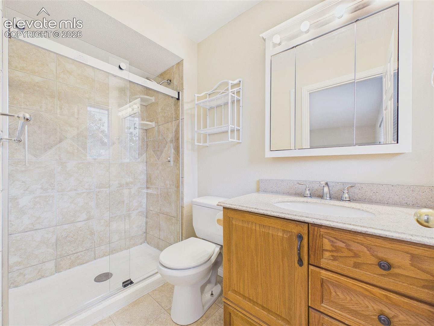 The ensuite bath features a granite-topped vanity, updated lighting, and a beautifully tiled walk-in shower with a frameless glass enclosure.