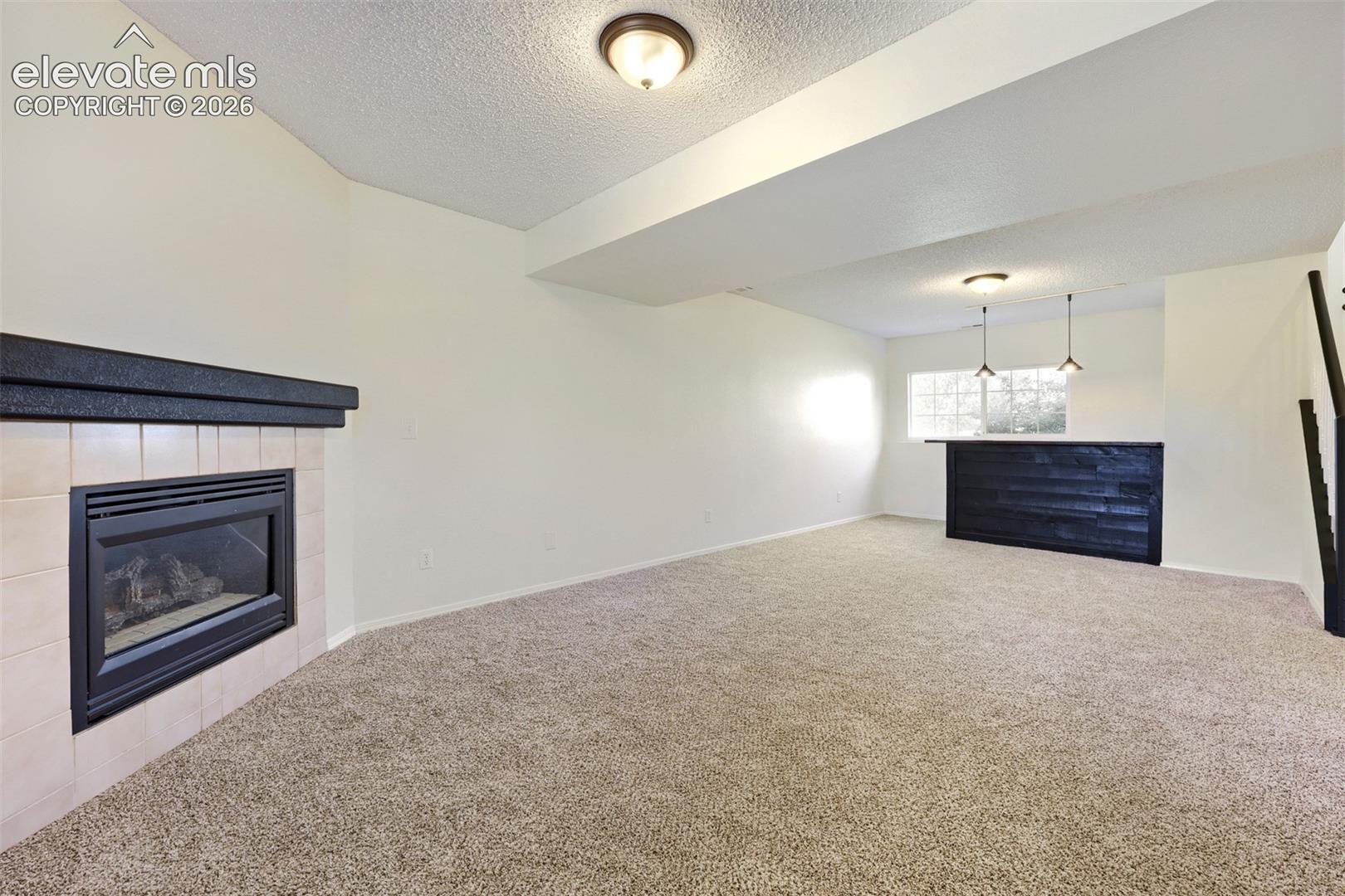 Spacious room featuring carpeting, a built-in fireplace with a tiled surround, a bar with a dark wood-finish front, and pendant lighting