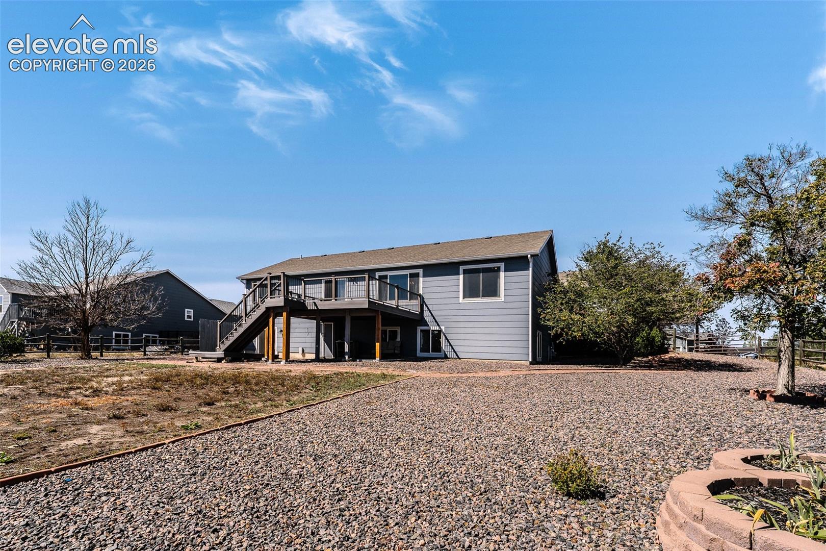 Spacious, fenced backyard with deck, patio, mature trees, grassy area, rock beds, and a garden shed.
