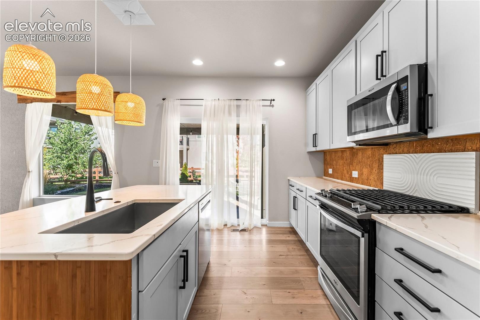 Kitchen featuring light-toned cabinetry, quartz countertops, a central island with an undermount sink and matte black faucet, and stainless steel appliances