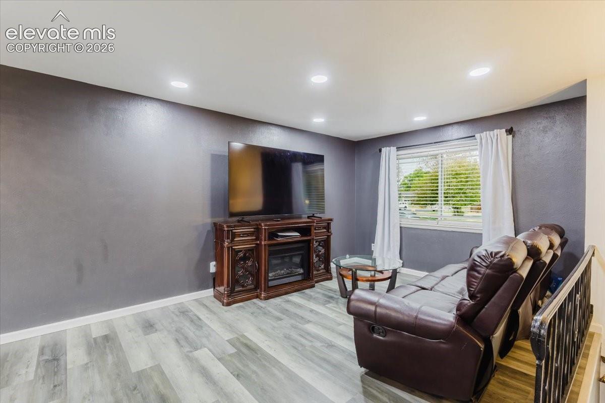 Living area featuring wood-finish flooring, recessed ceiling lighting, a window with blinds, and a built-in fireplace console