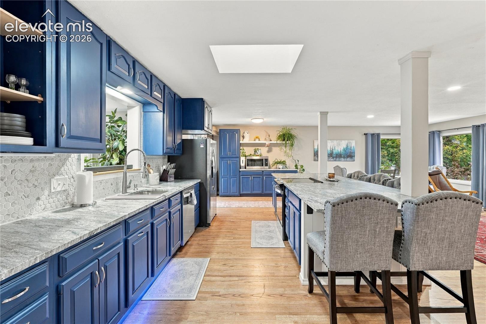 Kitchen featuring blue cabinetry, light-toned stone countertops, an expansive center island, wood-finish flooring, and a recessed ceiling light