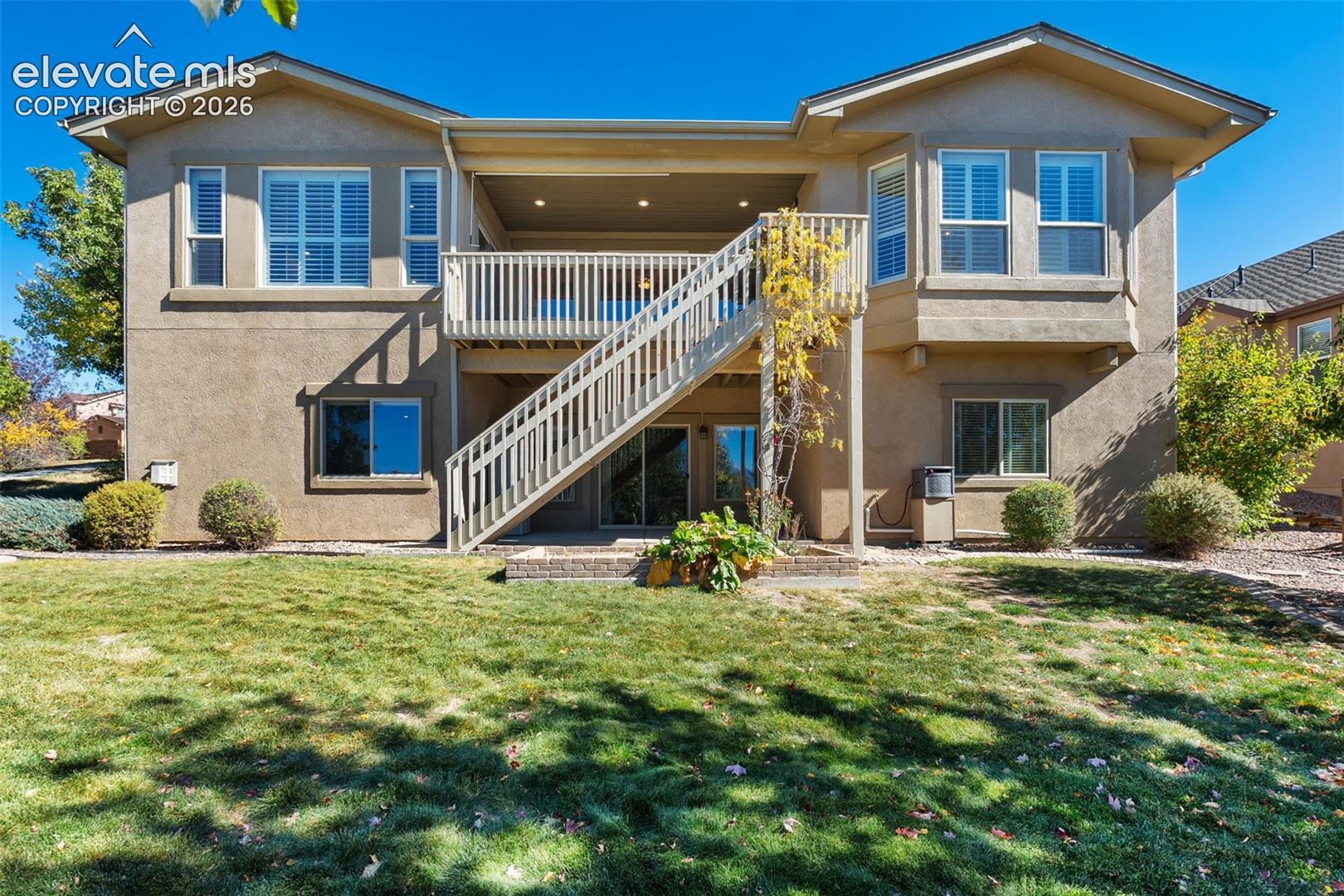 BACK OF HOME WITH LANDSCAPED LAWN & VIEW OF DECK AND PATIO