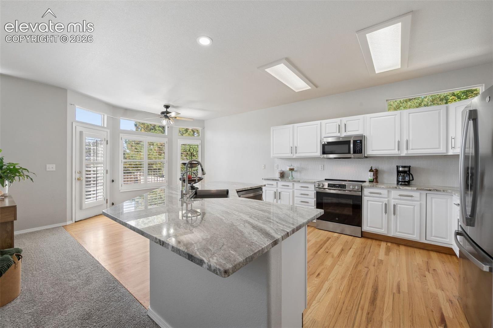 Kitchen featuring stone-topped center island with integrated sink, white cabinetry, stainless steel appliances, wood-finish flooring, and recessed ceiling lighting