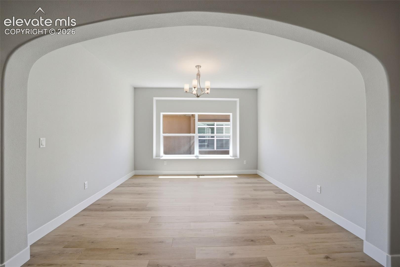Arched entryway featuring wood-finish flooring, a multipane window, and a multi-arm chandelier