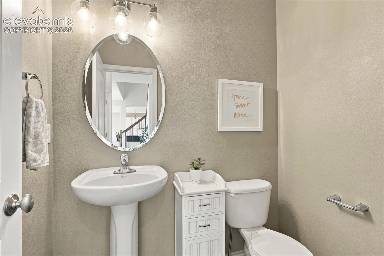 Oval mirror with polished edges, white pedestal sink, three-light vanity fixture with clear glass globes, and chrome hardware