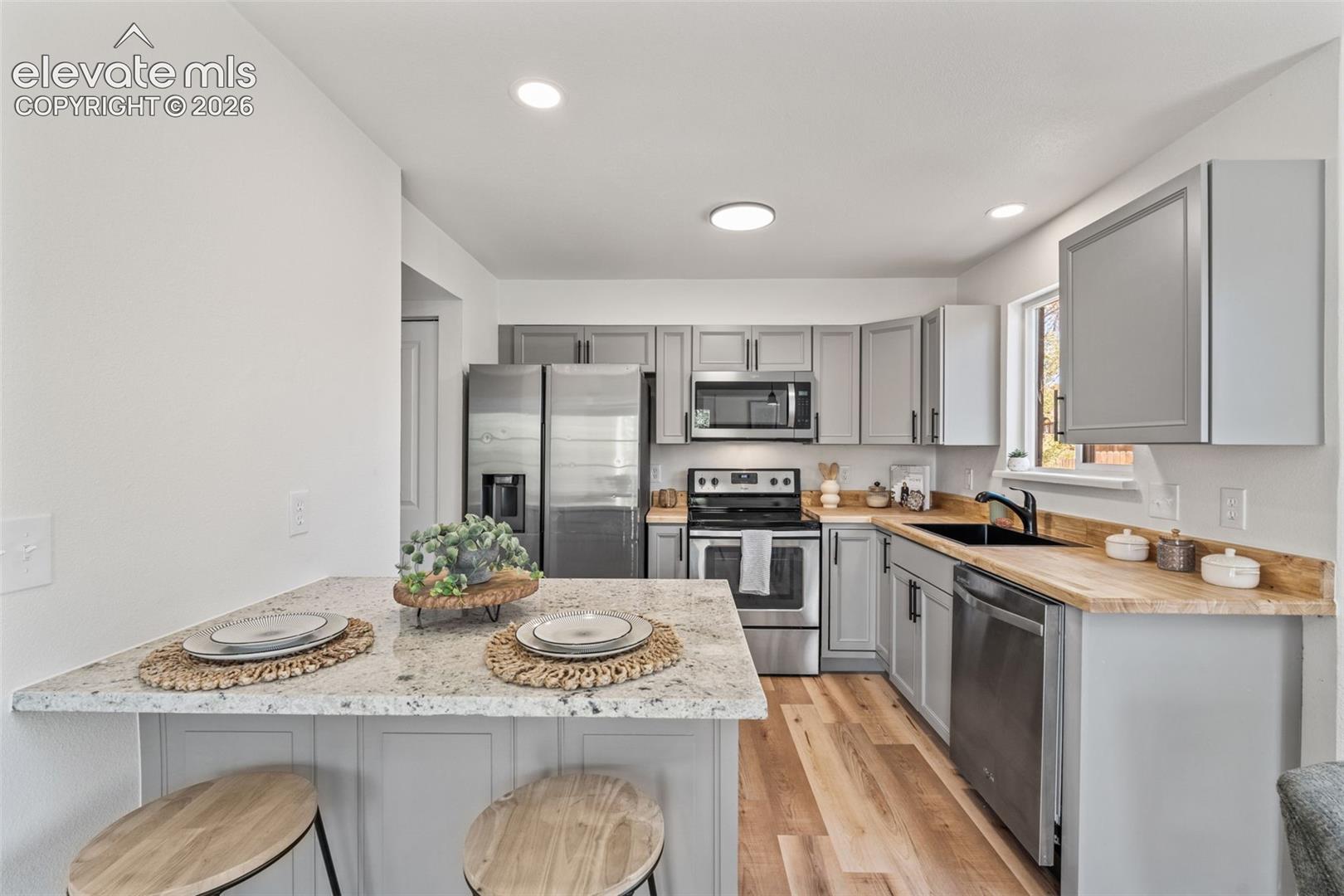Kitchen featuring light gray cabinetry, speckled stone countertops, wood-finish flooring, stainless steel appliances, and a peninsula with integrated seating