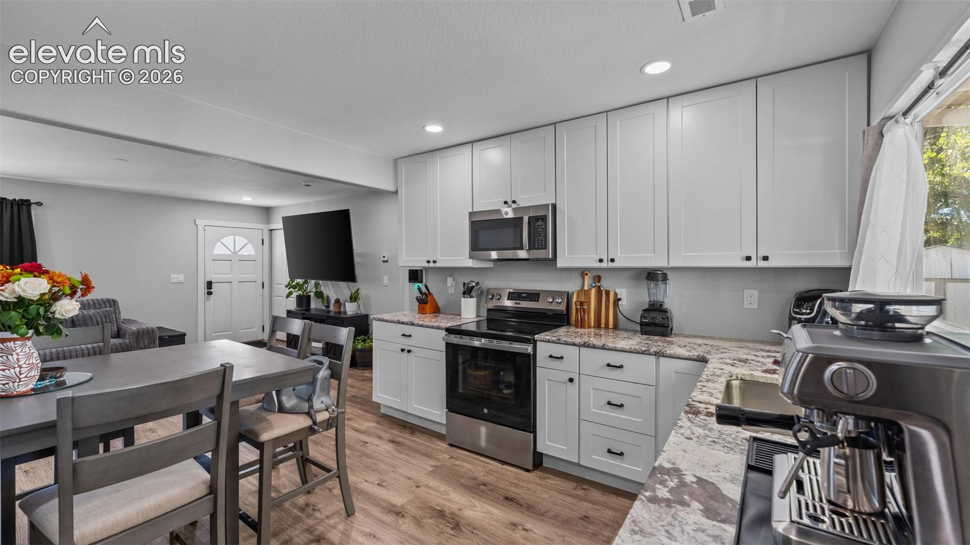 Kitchen featuring white shaker-style cabinetry, stone-patterned countertops, stainless steel appliances, recessed lighting, and wood-finish flooring