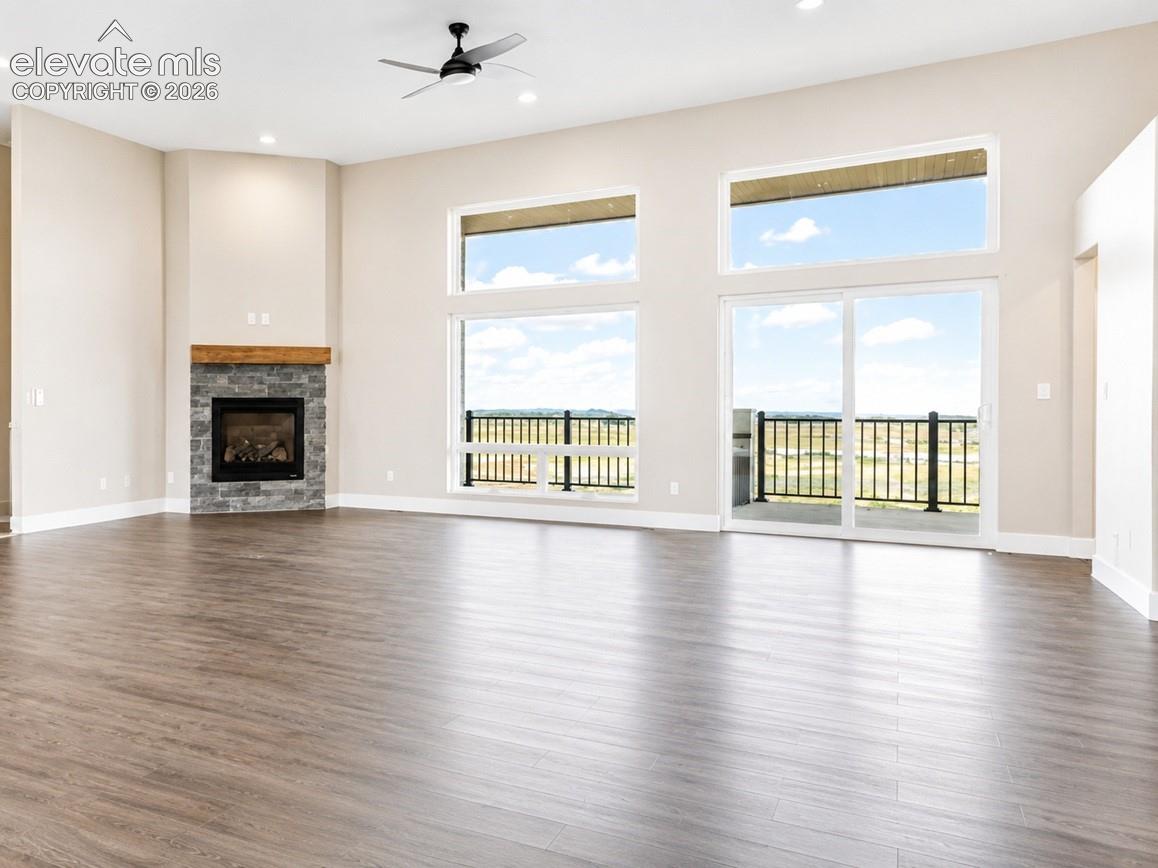 Spacious interior featuring wood-finish flooring, a stone fireplace with a wood mantle, and a ceiling fan