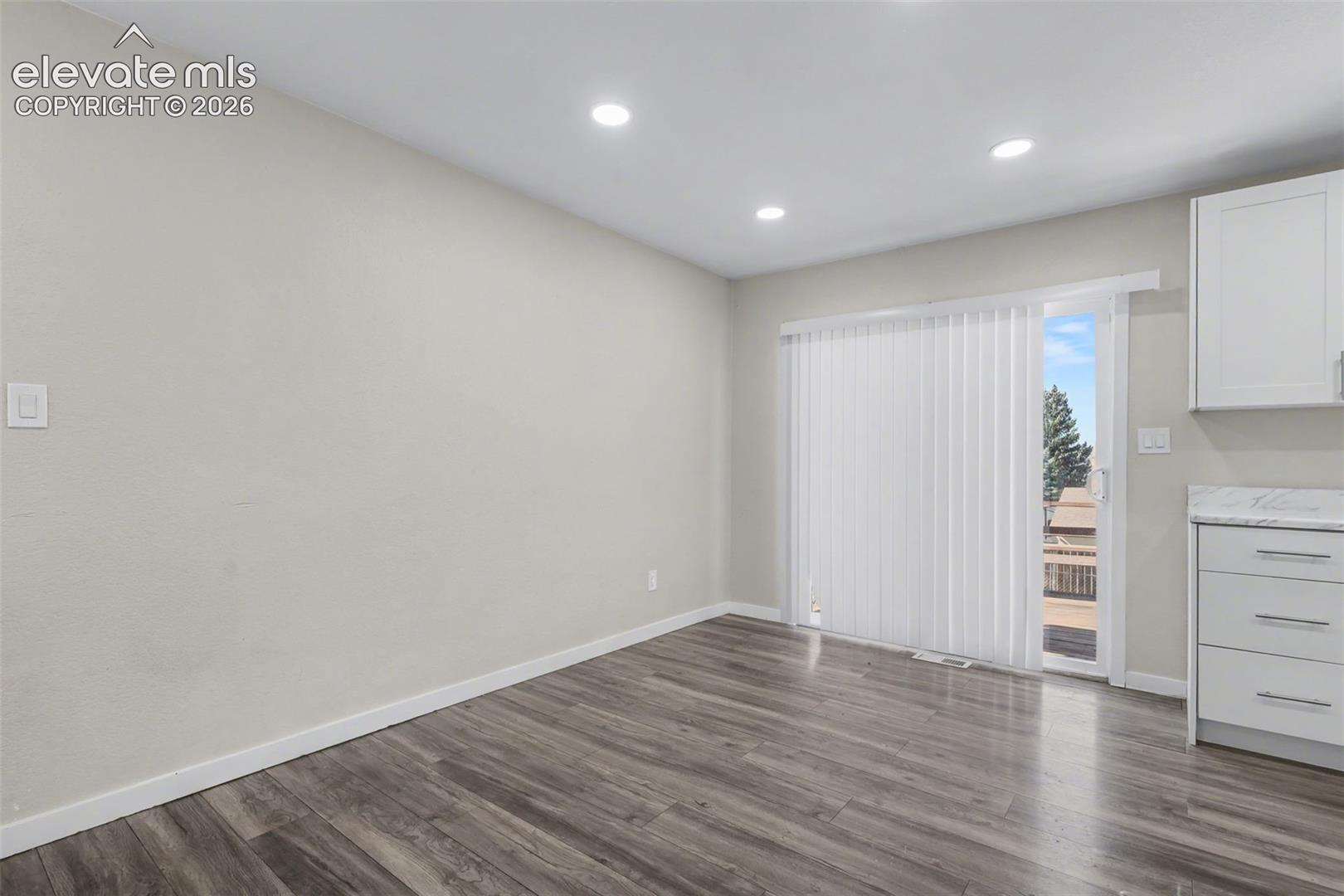 Wood-finish flooring, recessed lighting, sliding glass door, white cabinetry, and stone-patterned countertop