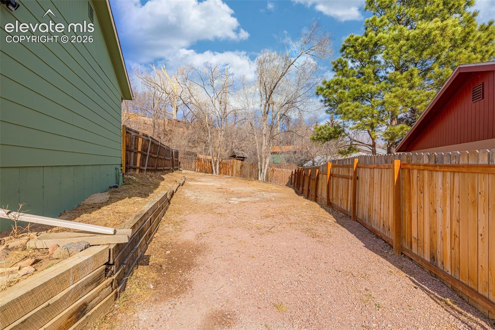 Gravel side yard featuring a timber retaining wall and vertical wood privacy fencing