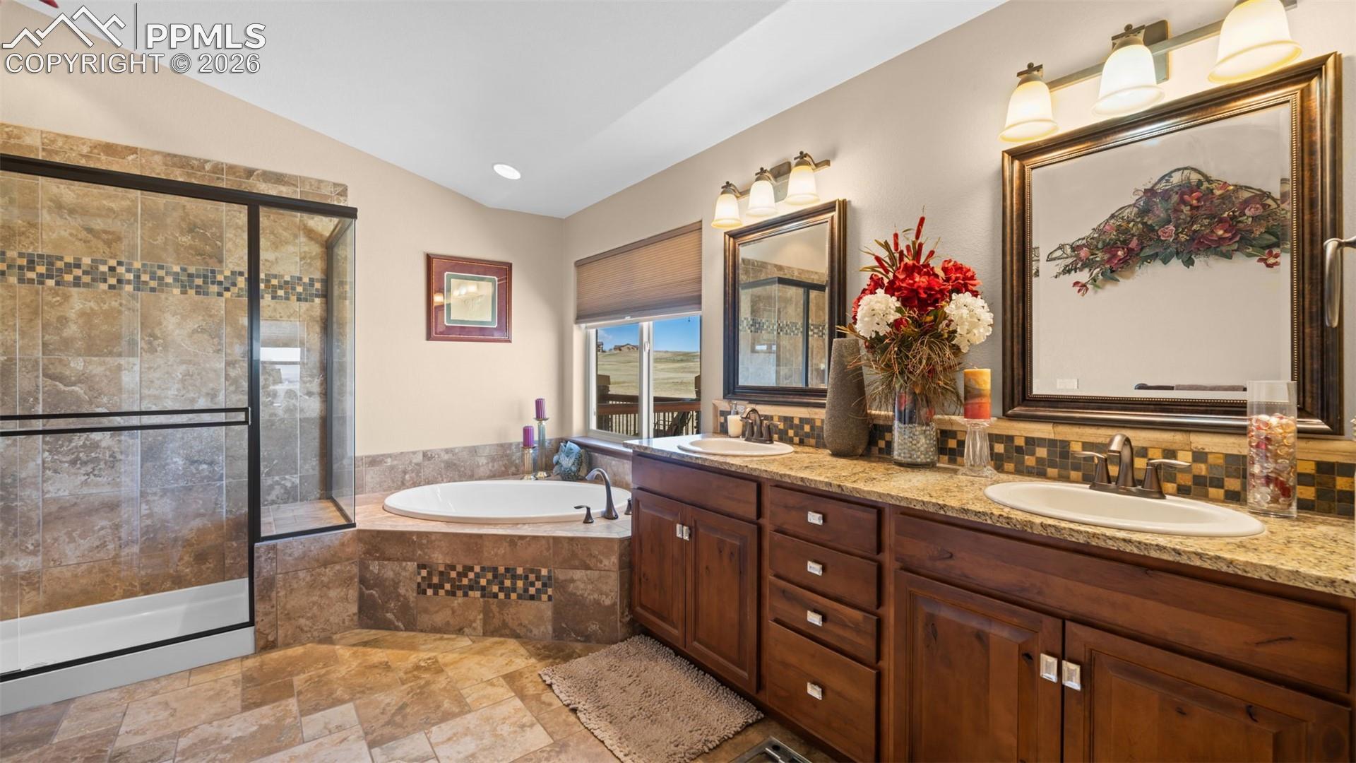 Bathroom with stone tile floors, double vanity, a bath, a stall shower, and vaulted ceiling