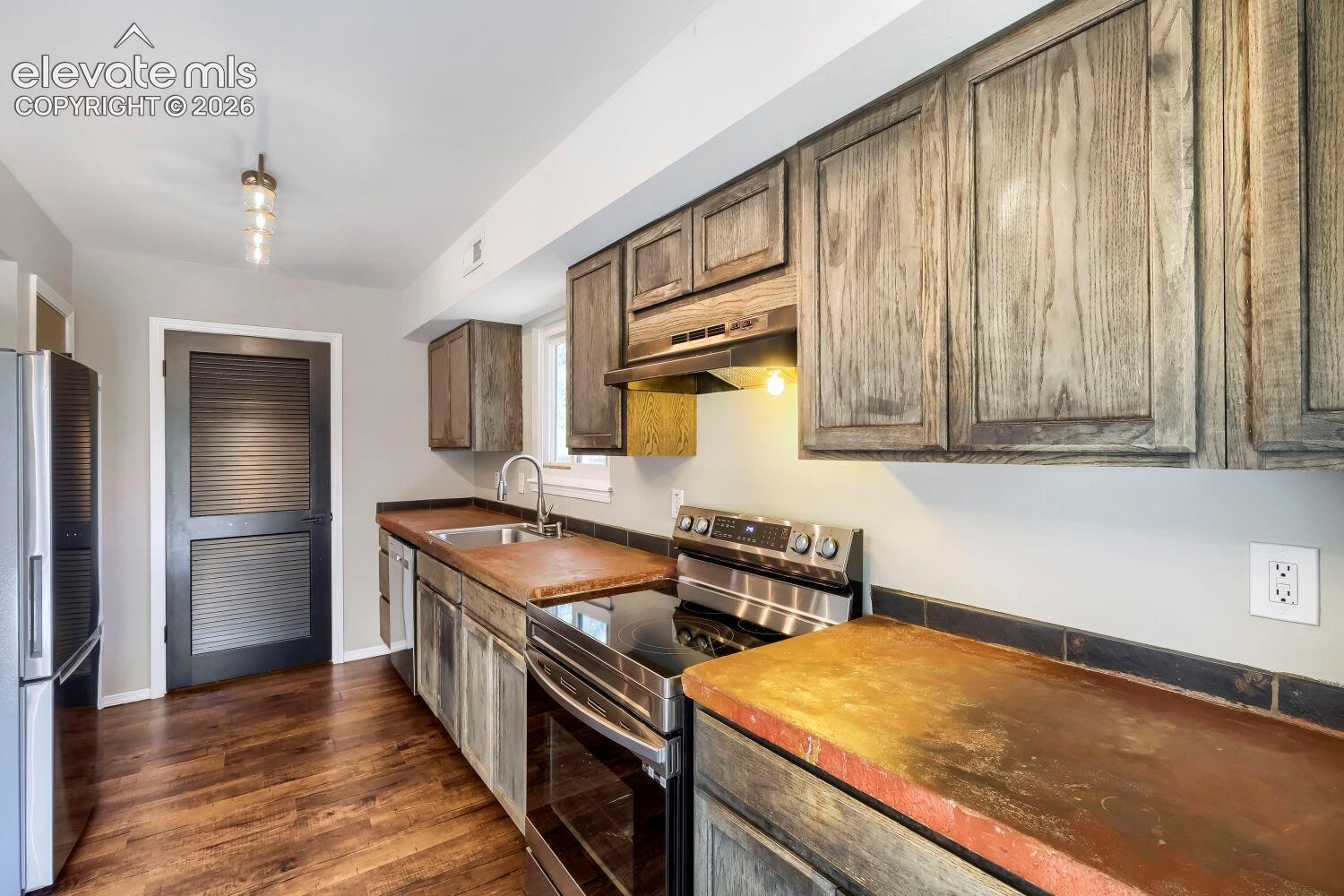 Kitchen featuring wood-finish flooring, stainless steel appliances, dark wood-grain cabinetry, and a dark tile backsplash
