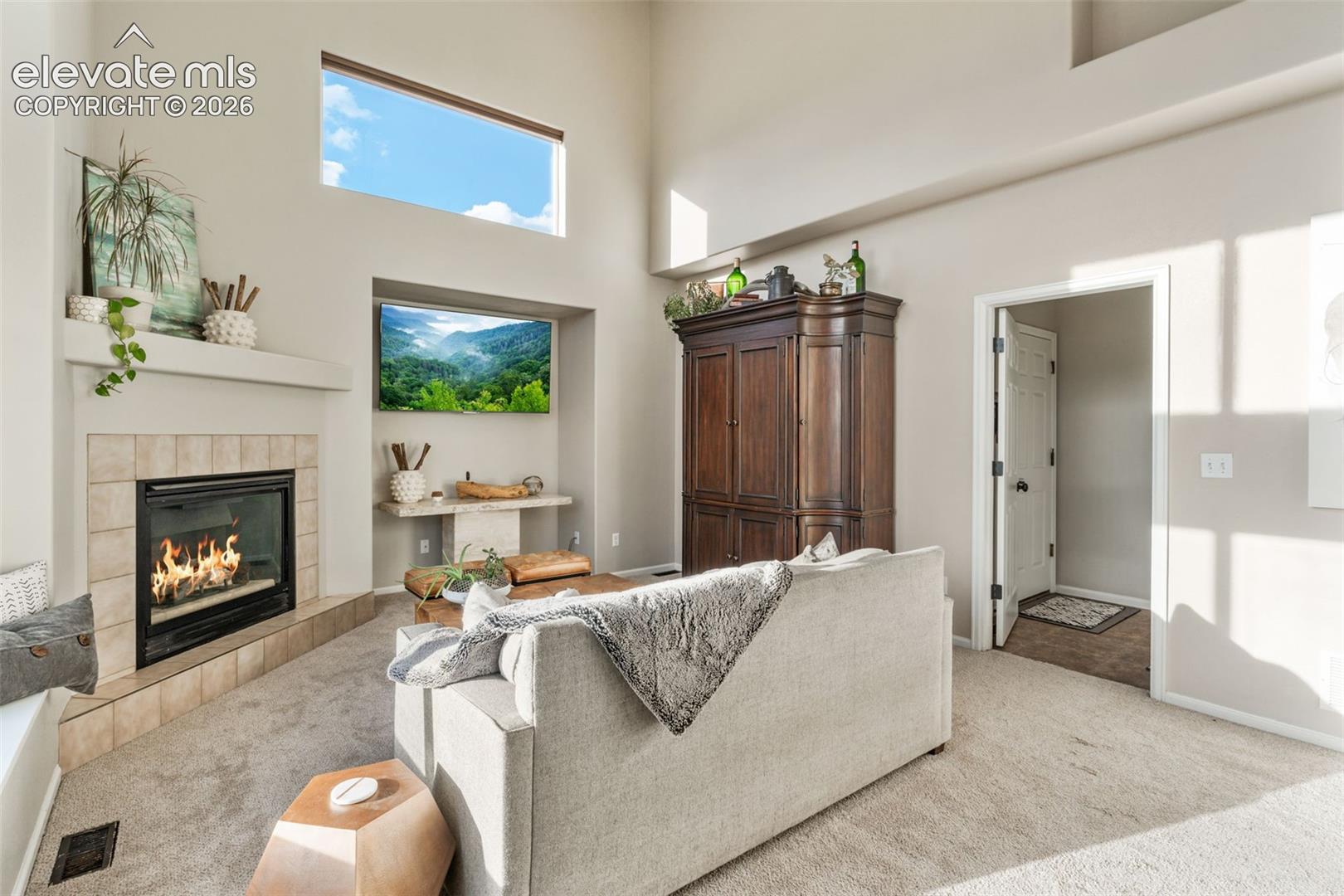 Vaulted ceilings, fireplace with tile surround, built-in shelving alcove, and transom windows