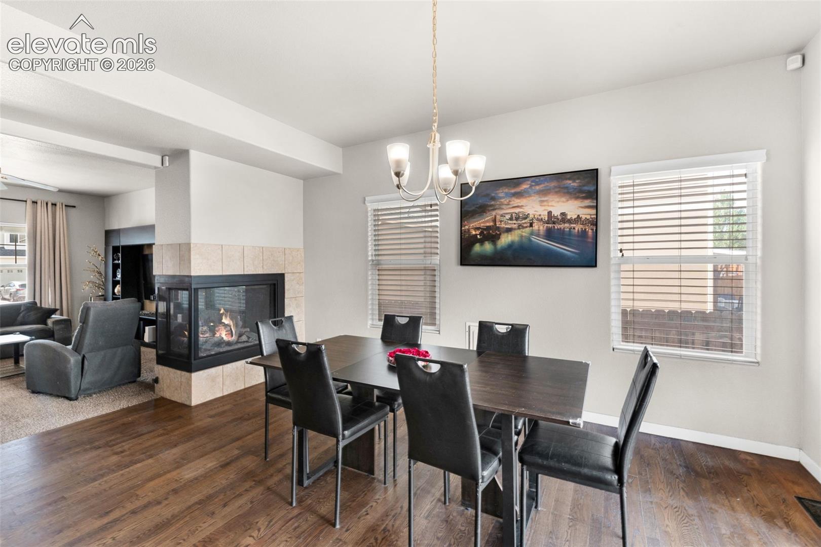 Dual-sided fireplace with tile surround, wood-finish flooring, and multi-arm chandelier fixture