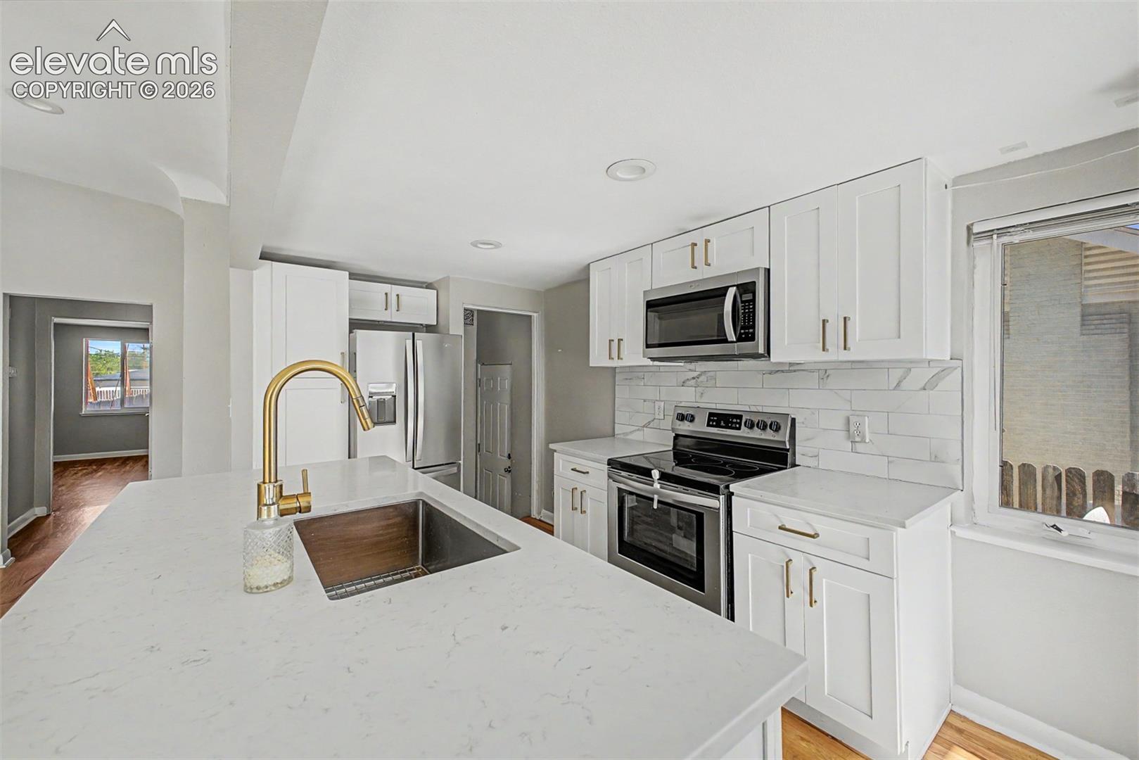 Kitchen featuring a central island with white cabinetry, gold-toned hardware, an integrated sink, and a gold-toned faucet