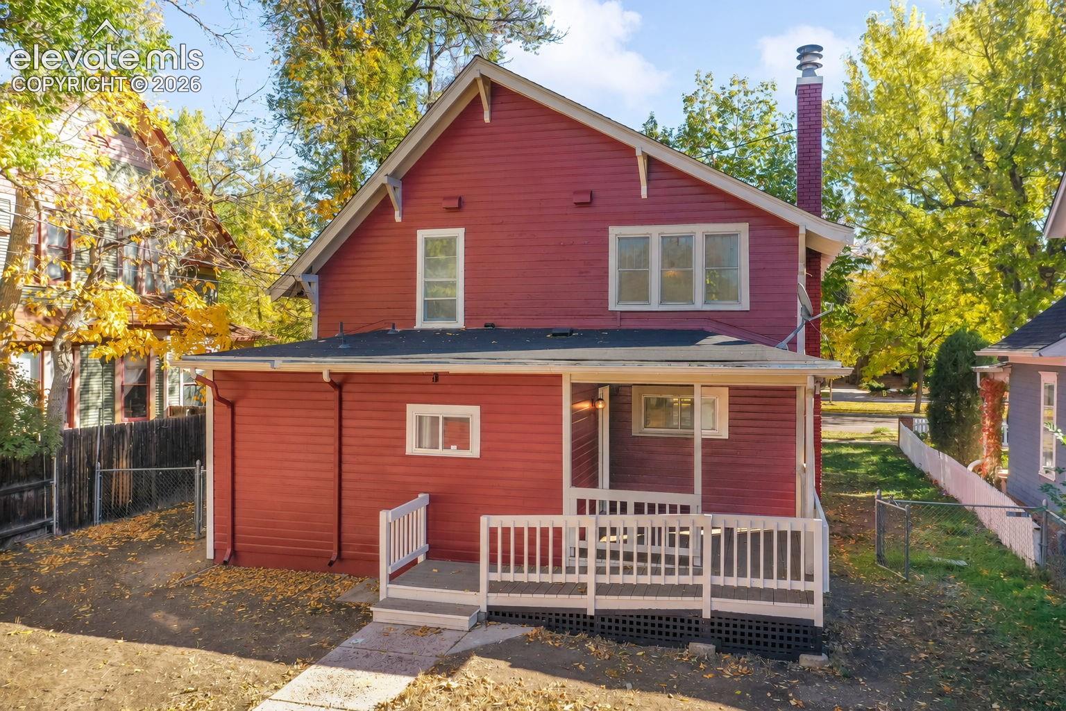 Exterior featuring red horizontal siding, a masonry chimney, a rear covered porch, and a raised wooden deck with railings