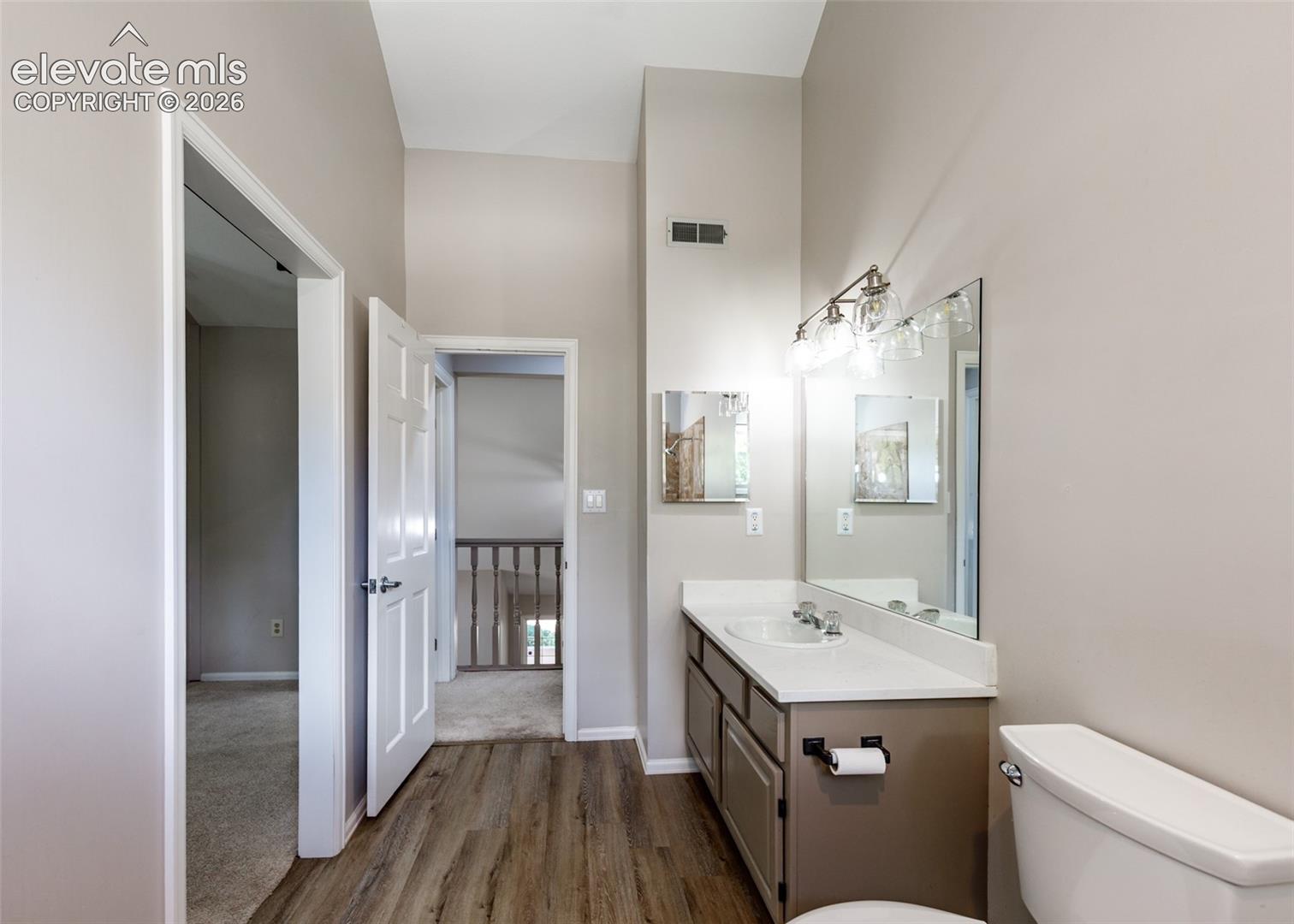 Bathroom featuring wood-finish flooring, a single vanity with a white countertop and integrated sink, and an overhead vanity light fixture