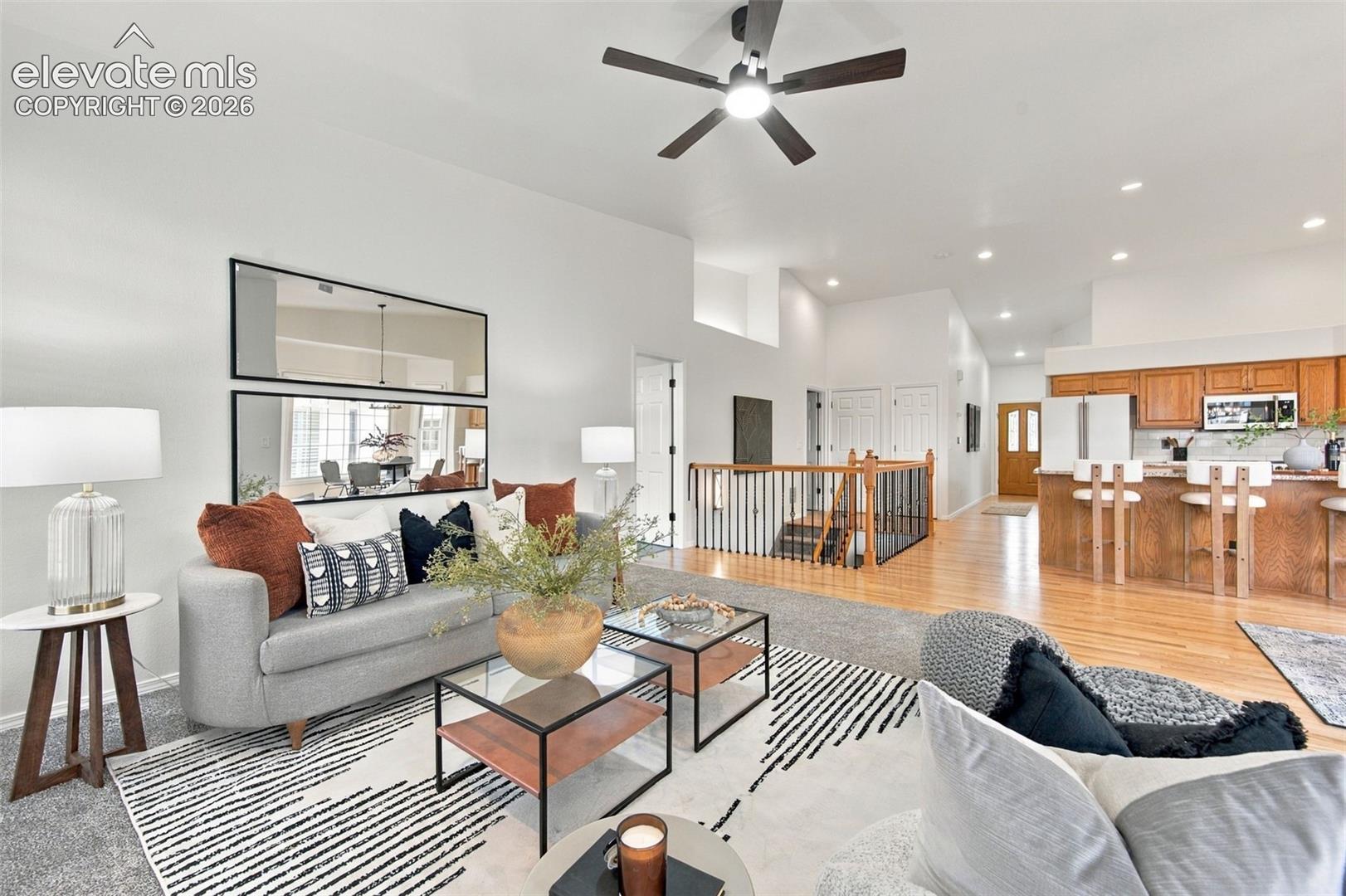 Open-concept living space featuring vaulted ceilings, wood-finish flooring, a tiered staircase with a wood and metal railing, and built-in wooden cabinetry in the kitchen