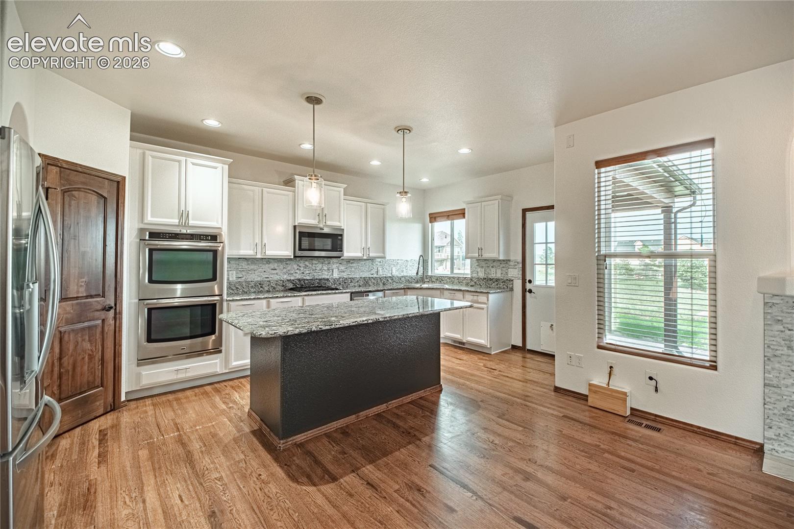 Open-concept kitchen with wood-finish flooring, white cabinetry, and stainless steel double ovens
