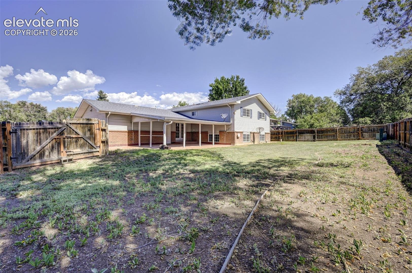 Exterior elevation featuring brick and horizontal siding, covered rear patio, and expansive grounds enclosed by perimeter wood fencing