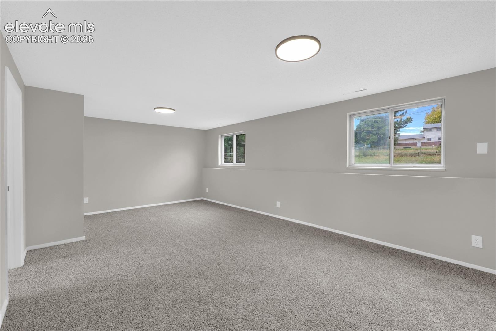 Spacious room featuring neutral carpeting, light gray walls, and two flush-mount ceiling lights