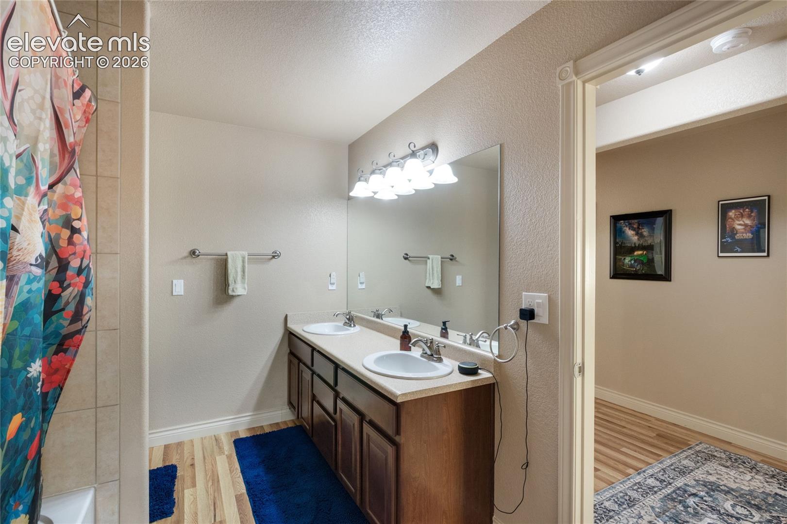 Basement Bathroom featuring a double vanity with wood-finish cabinetry, a full-width vanity mirror, a five-light vanity fixture, and dual integrated sinks with chrome faucets