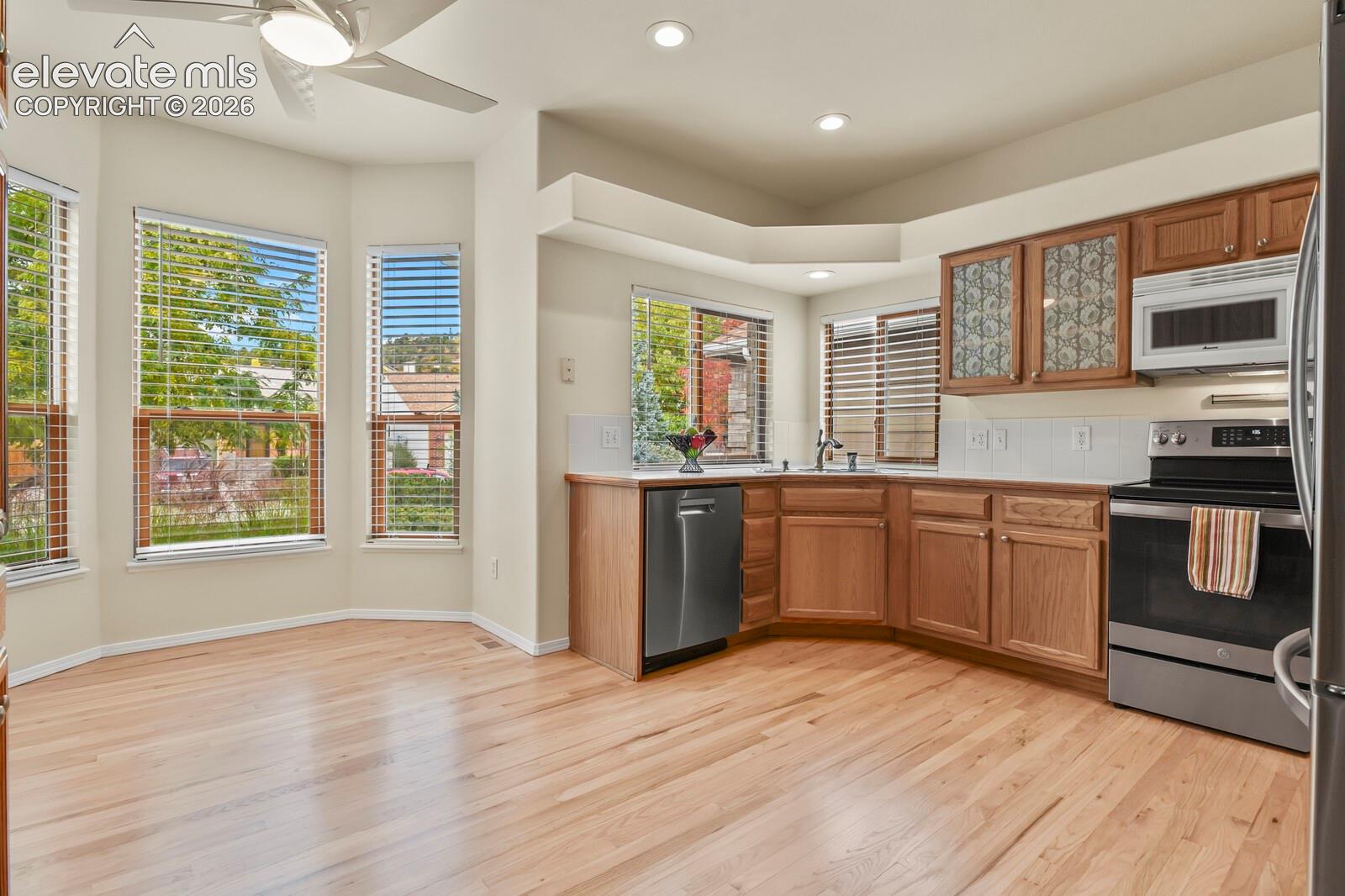 Kitchen featuring wood cabinetry, stainless steel appliances, bay window, recessed lighting, and wood-finish flooring