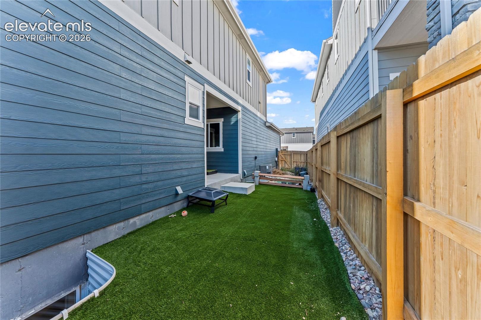 Spacious backyard oasis featuring lush synthetic turf, wooden privacy fencing, and gravel landscaping accents