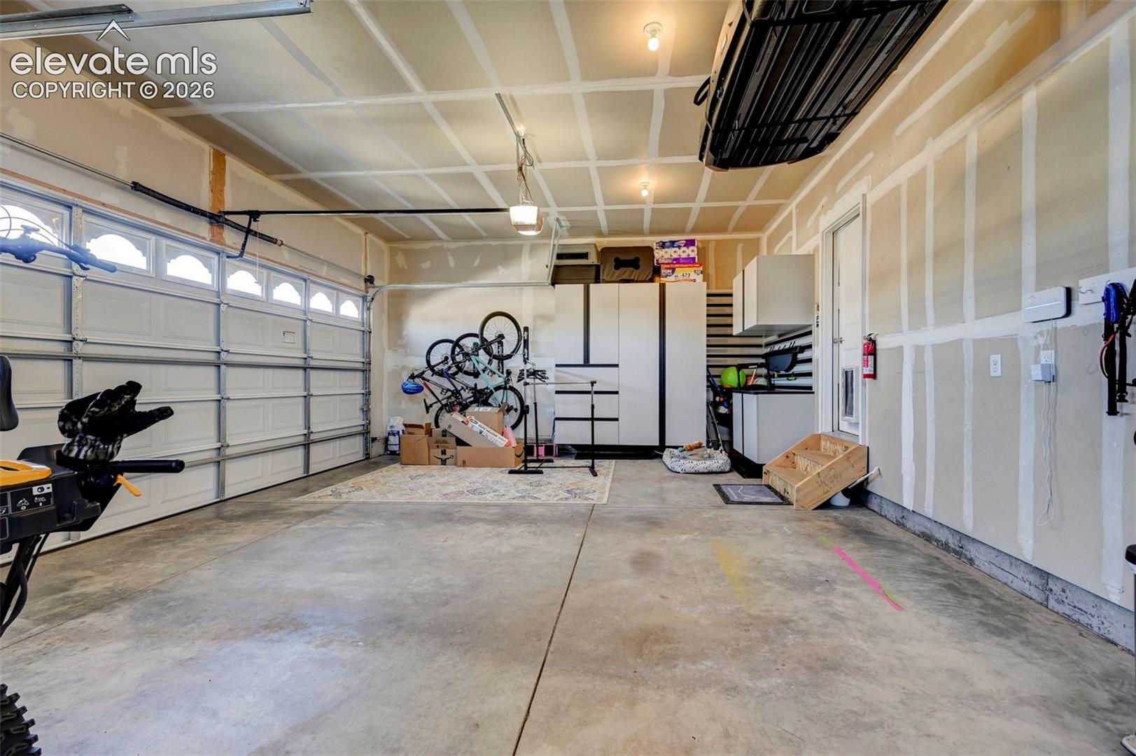 Spacious garage featuring a concrete floor, two overhead garage doors with frosted window inserts, exposed ceiling joists, and overhead lighting