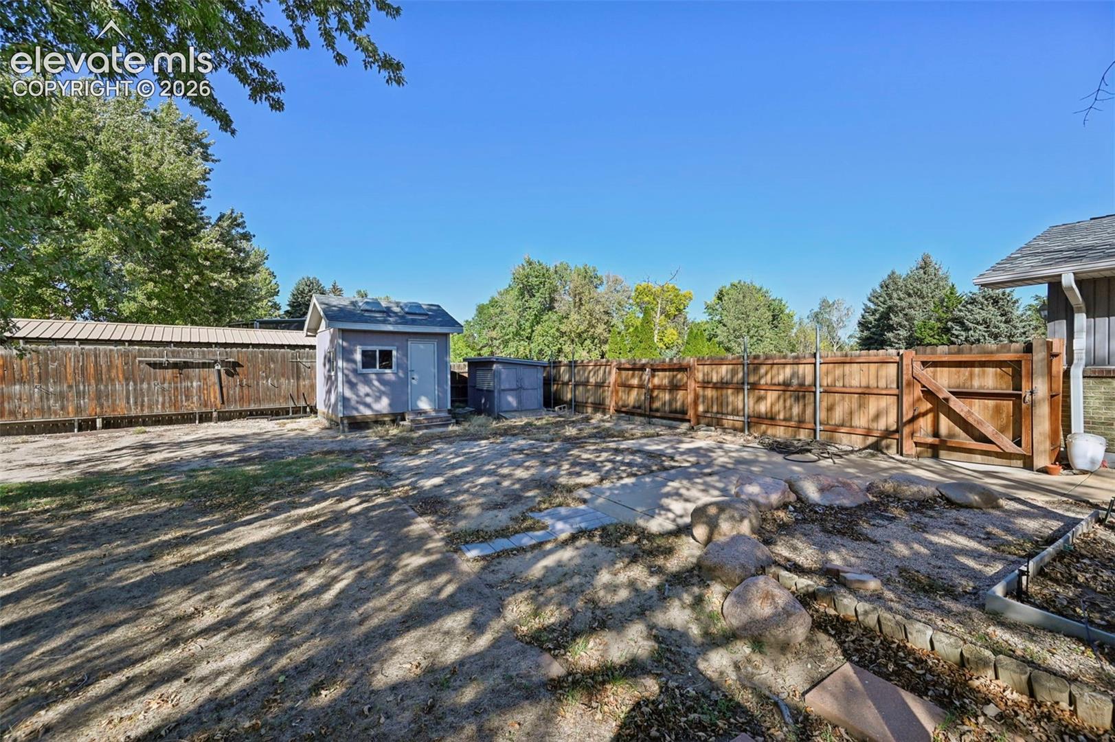 Expansive outdoor space featuring a wood privacy fence, a detached storage shed, a secondary utility shed, and a patio area