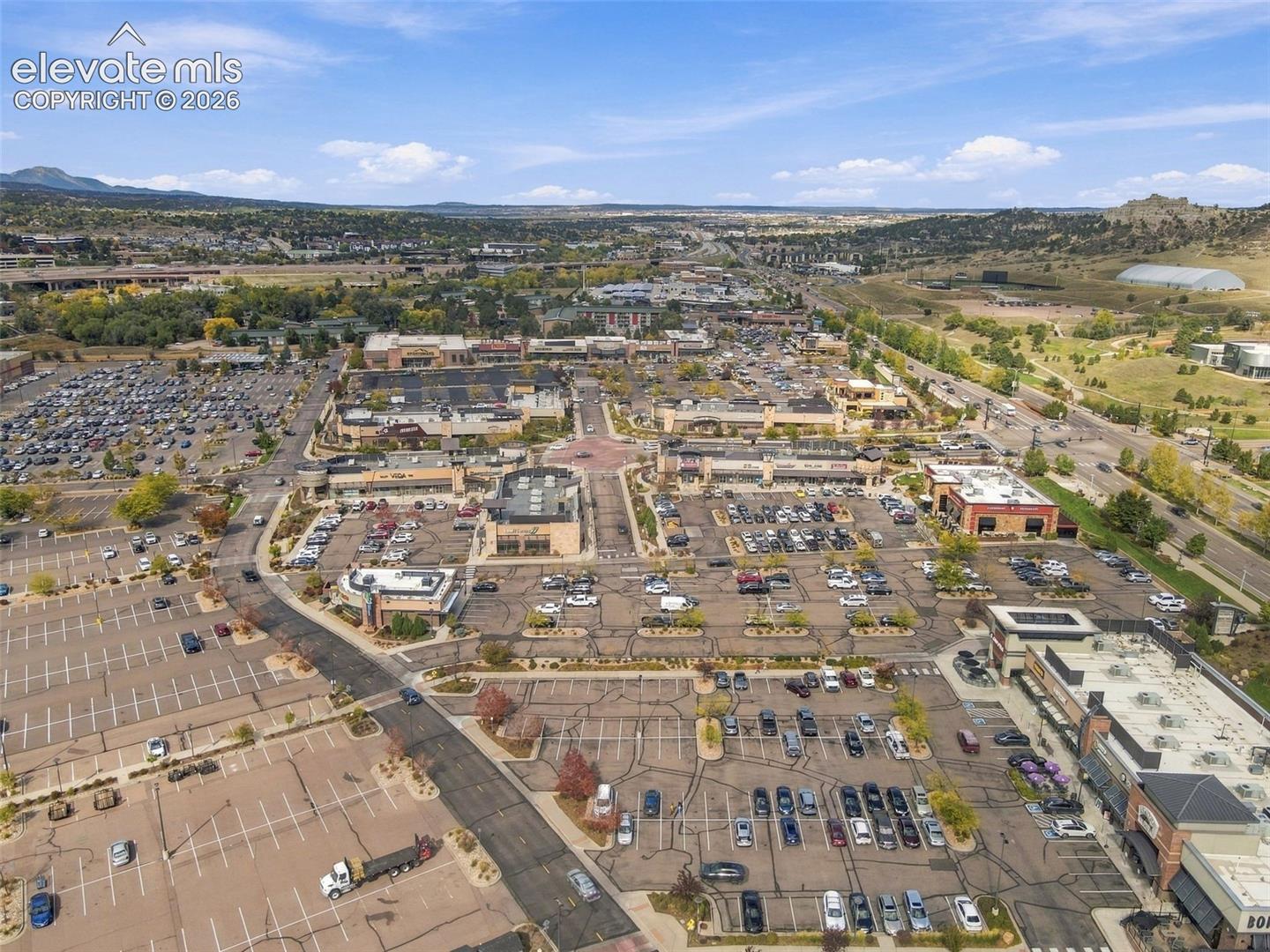Aerial perspective of a multi-building commercial plaza featuring extensive paved parking surfaces and mountain backdrops