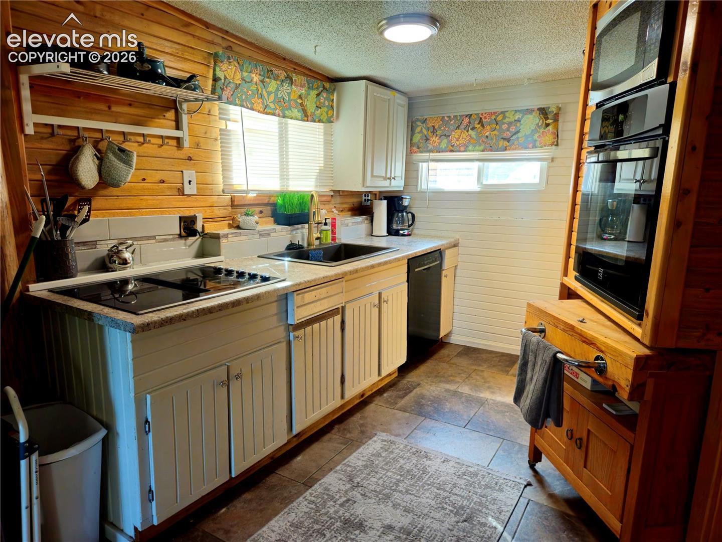 Main house Kitchen featuring wood-paneled walls, white cabinetry, integrated cooktop, wall oven, and built-in microwave