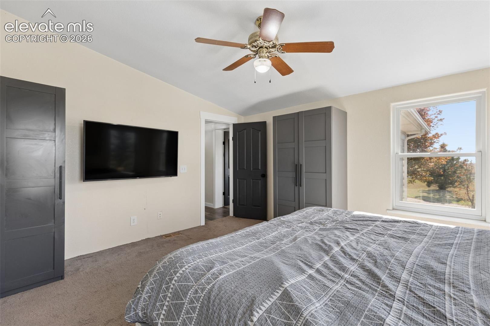 Vaulted ceiling featuring a central multi-blade ceiling fan, paneled dark-finish doors, and a double-hung window