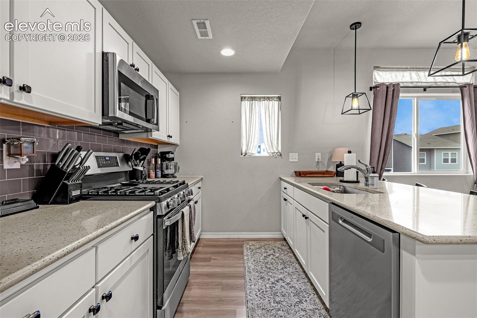 Modern kitchen featuring white cabinetry, light-toned countertops, stainless steel appliances, a dark subway tile backsplash, and wood-finish flooring