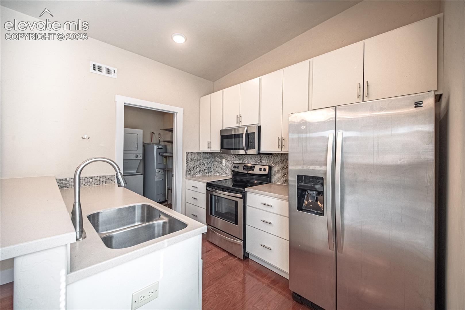 Kitchen featuring light cabinetry, stainless steel appliances, a mosaic tile backsplash, and a double basin sink with a gooseneck faucet