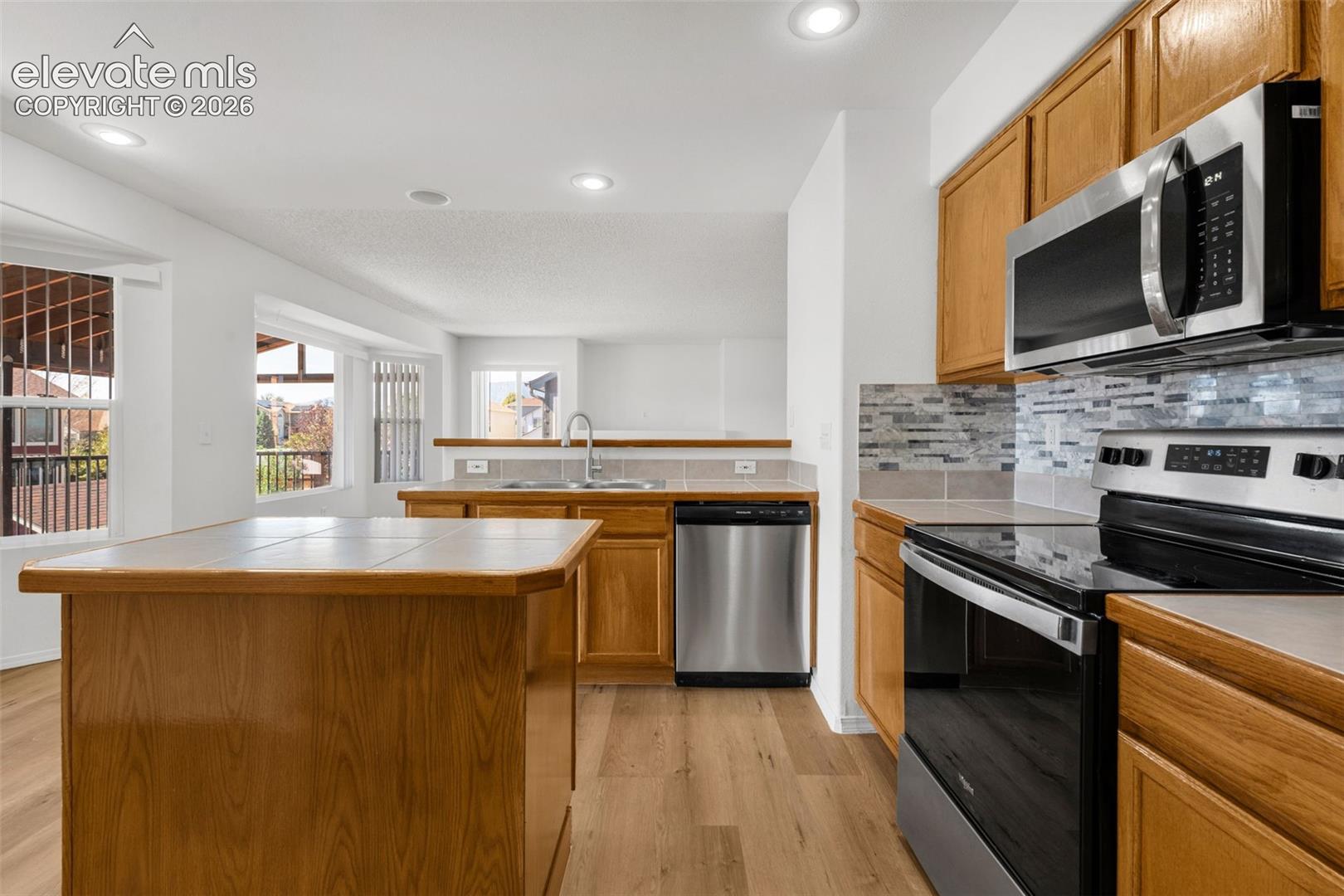 Wood-finish flooring throughout, stainless steel appliances, tile backsplash, and recessed lighting