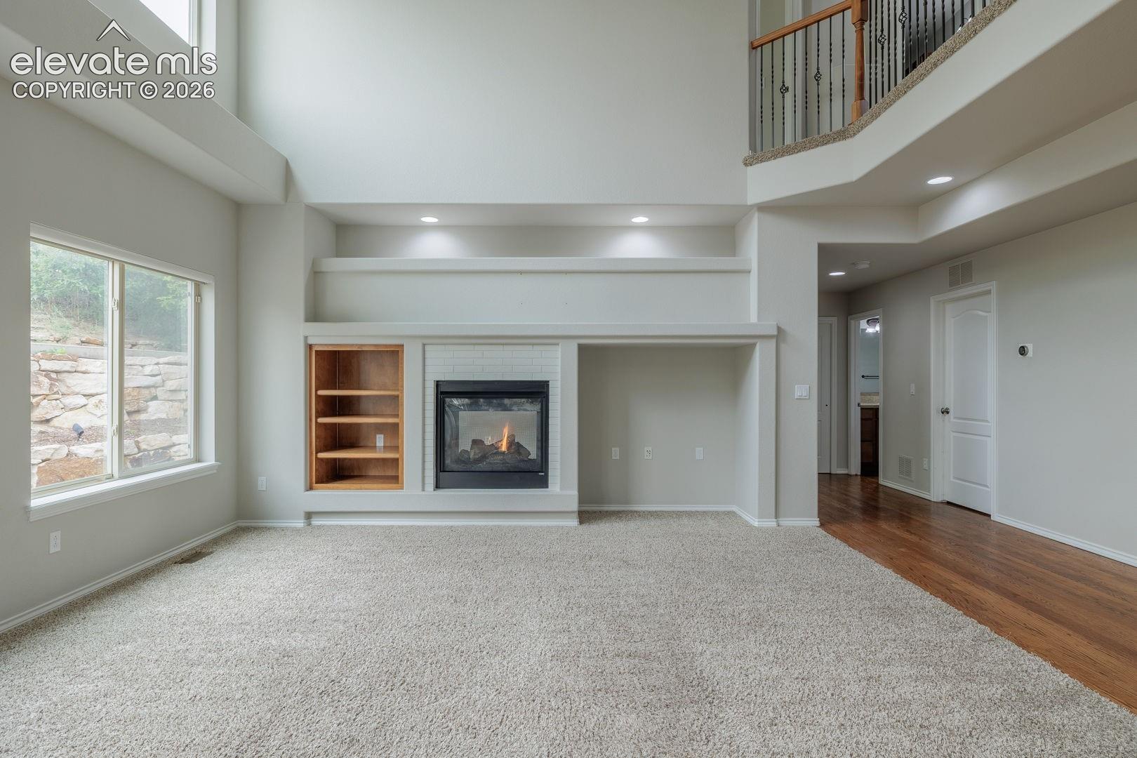 Spacious great room showcasing soaring ceilings, abundant natural light from large windows, and a striking built-in entertainment center with wood-finish cabinetry flanking a gas fireplace